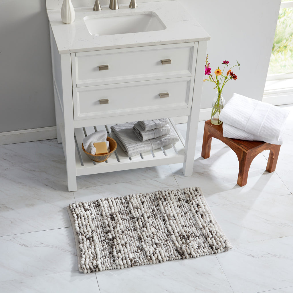 Space-dyed microfiber bath rug in neutral ivory and gray tones placed in front of a bathroom vanity. The plush textured surface adds softness, absorbency, and comfort underfoot while complementing the bright, modern bathroom décor.