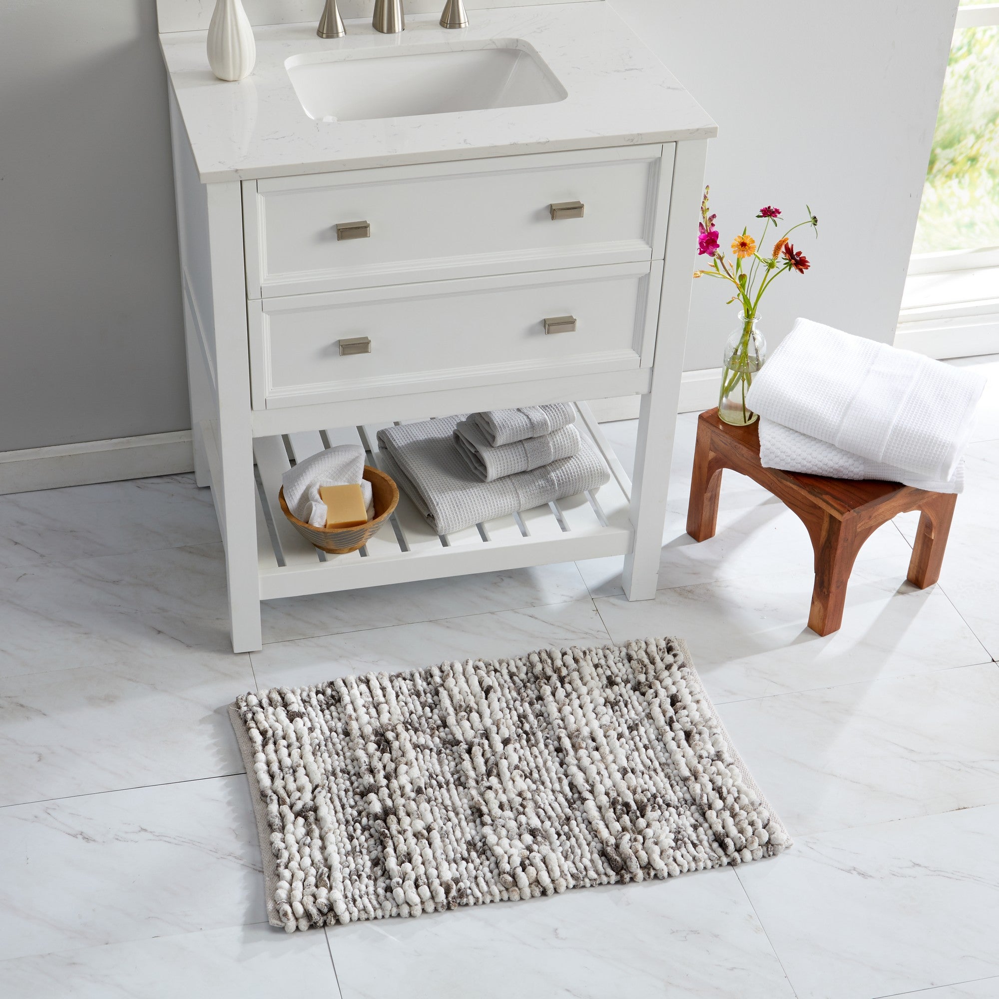 Space-dyed microfiber bath rug in neutral ivory and gray tones placed in front of a bathroom vanity. The plush textured surface adds softness, absorbency, and comfort underfoot while complementing the bright, modern bathroom décor.