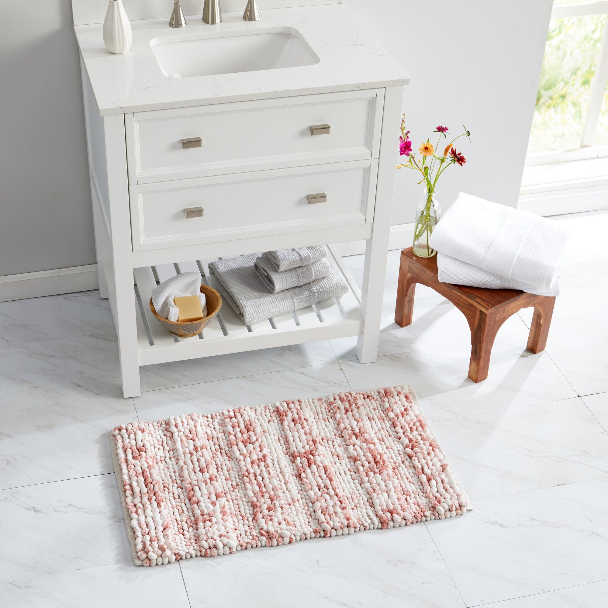 Space-dyed microfiber bath rug in soft blush pink and ivory tones placed in a bright bathroom setting. The plush pebble-textured design adds comfort, absorbency, and a subtle touch of color, complementing modern and farmhouse-inspired décor styles.