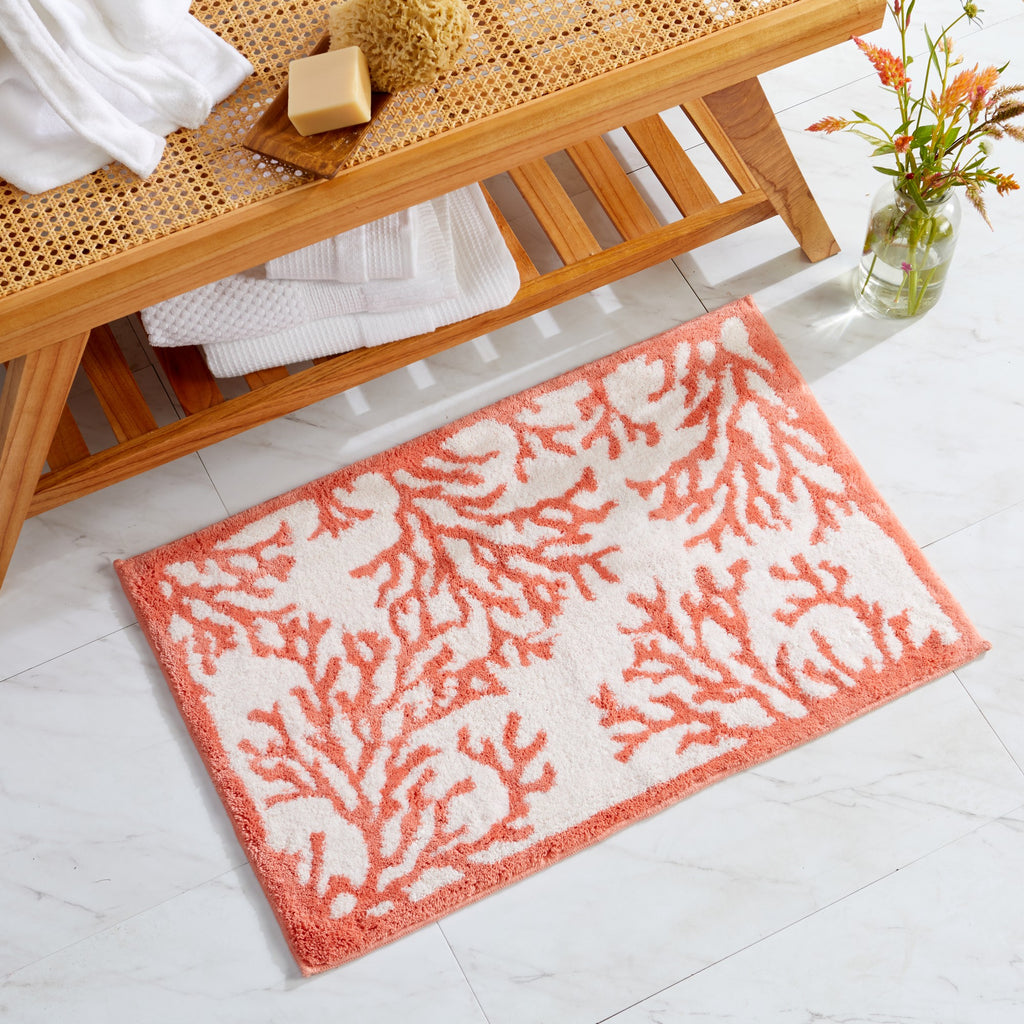 A coastal themed printed bath rug with a coral design in orange and white colors, placed on a bathroom floor.