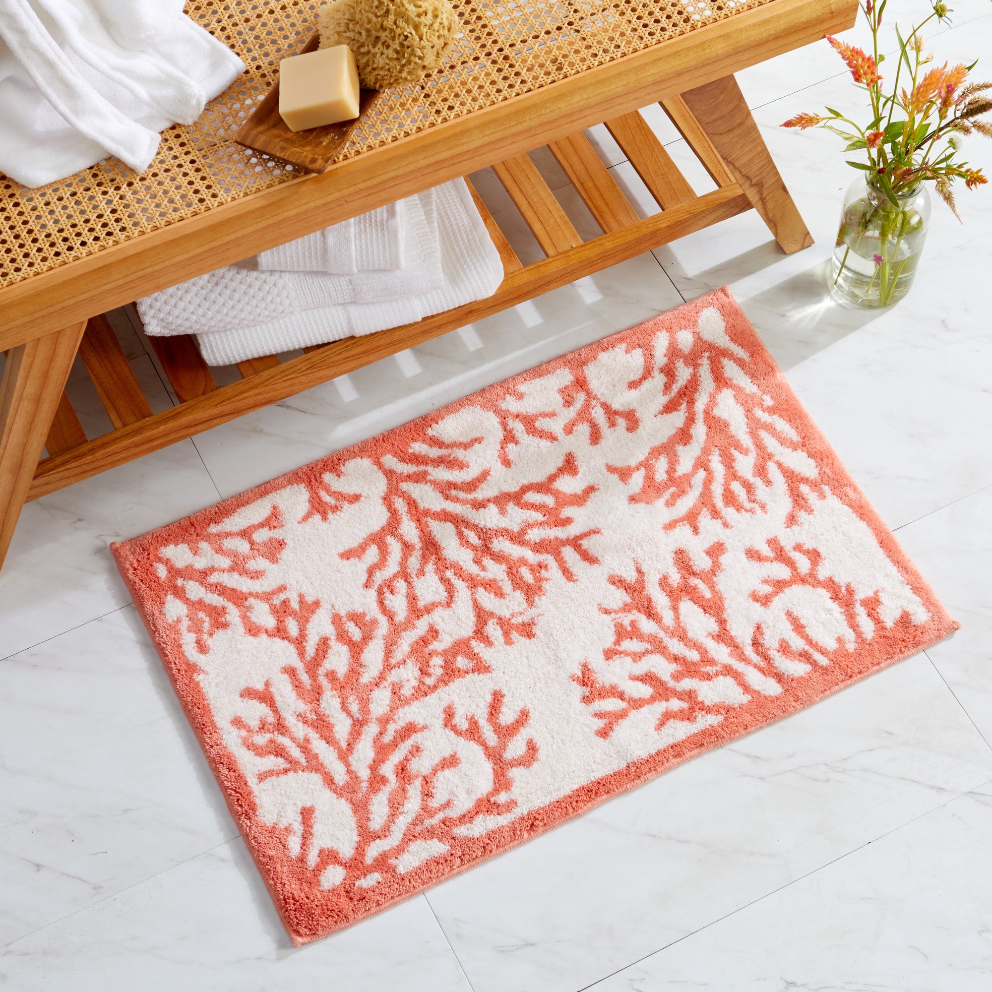 A coastal themed printed bath rug with a coral design in orange and white colors, placed on a bathroom floor.