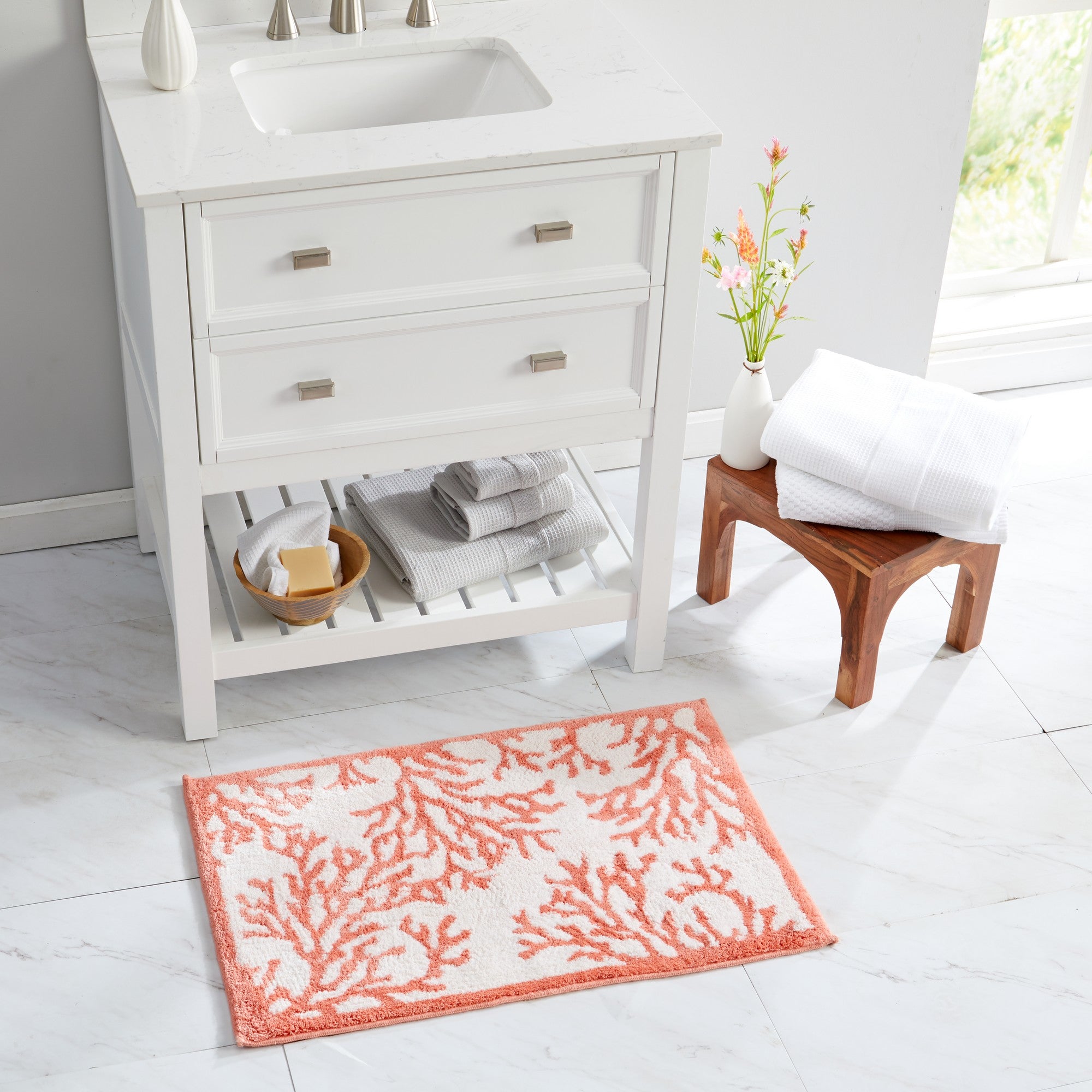 Coastal-inspired bath rug featuring a coral branch pattern in soft coral pink and ivory tones, styled in a bright bathroom setting. The plush, absorbent rug adds seaside charm, comfort, and texture while complementing both coastal and contemporary bathroom décor.