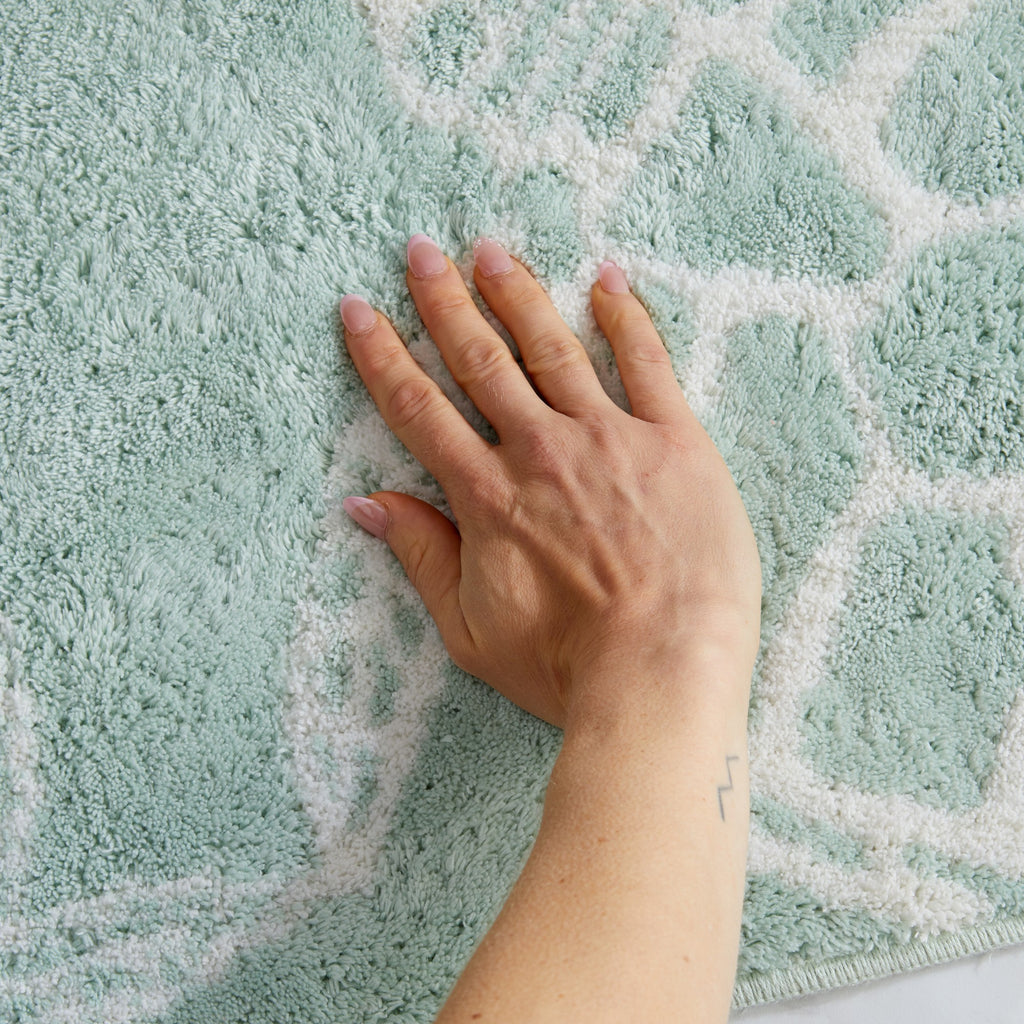 Close-up of a plush coastal bath rug featuring a sea turtle shell pattern in white on a soft seafoam green background. The image highlights the rug’s thick, absorbent pile and soft texture for added comfort underfoot.