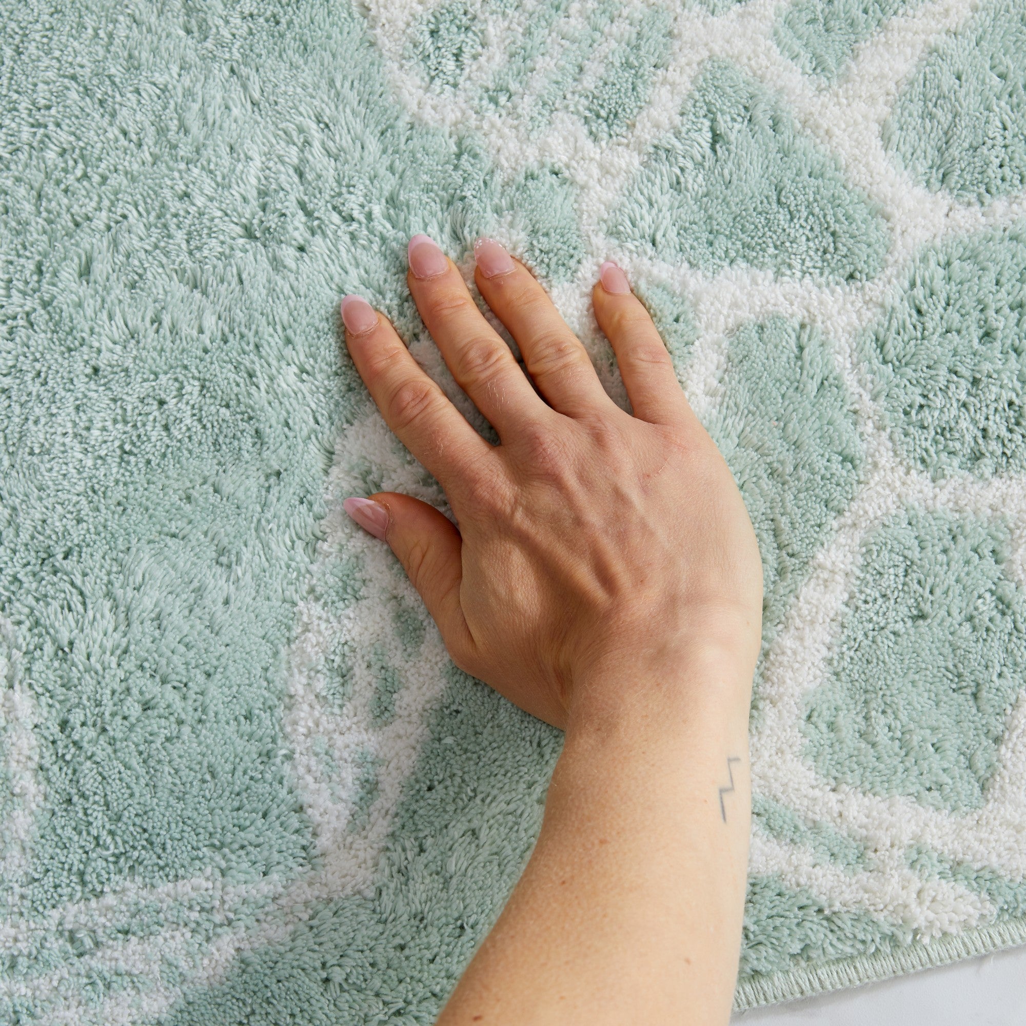 Close-up of a plush coastal bath rug featuring a sea turtle shell pattern in white on a soft seafoam green background. The image highlights the rug’s thick, absorbent pile and soft texture for added comfort underfoot.