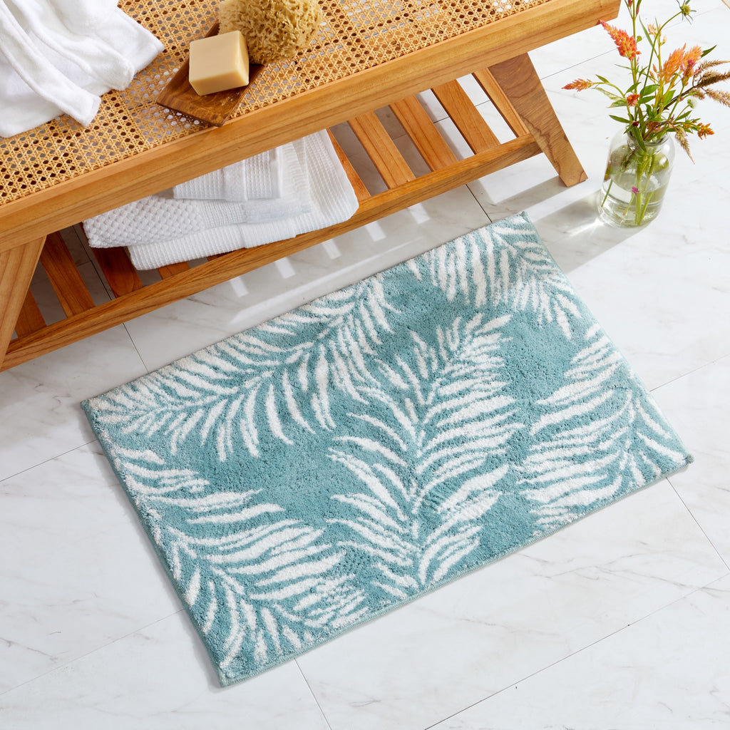 Tropical-inspired bath rug featuring white palm leaf silhouettes on a soft aqua blue background. The plush, absorbent design adds a fresh coastal feel while providing comfort, texture, and style to bathroom décor.