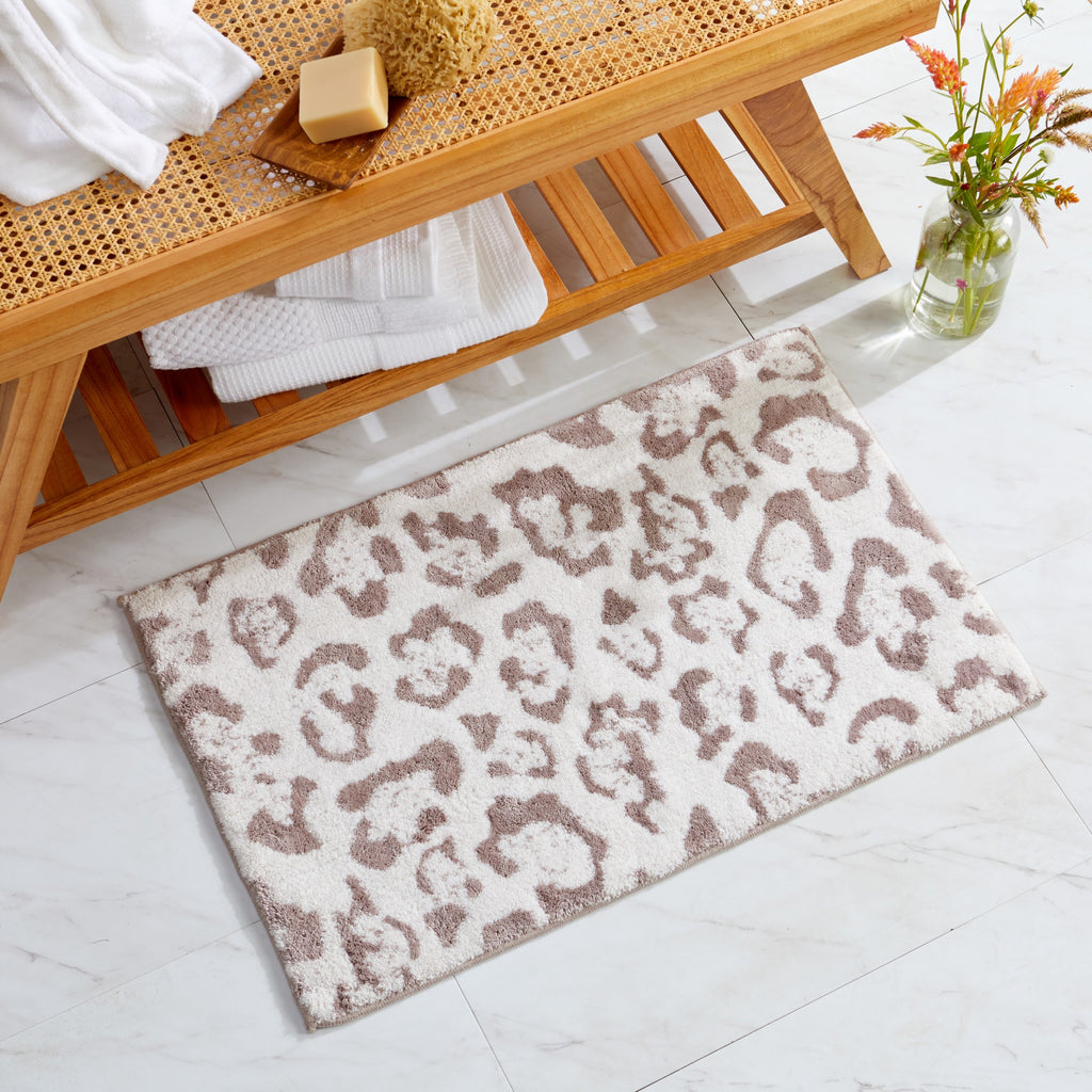 An animal-printed bath rug laid out on a tiled floor, with a wooden bench and various bathroom accessories in the background.