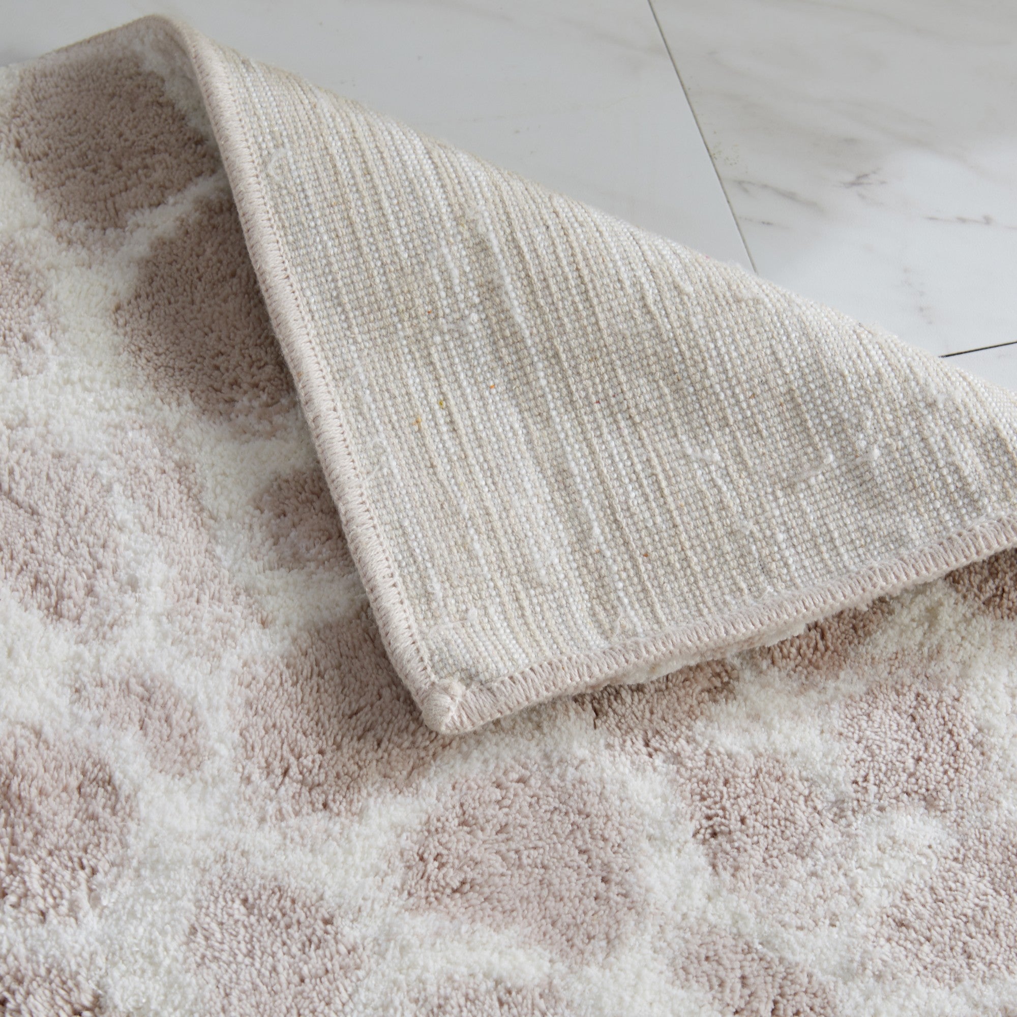 Close-up of a giraffe-print bath rug with a folded corner revealing the durable woven backing. The soft ivory and light taupe pattern highlights the plush texture, quality craftsmanship, and comfortable cushioning designed for everyday bathroom use.