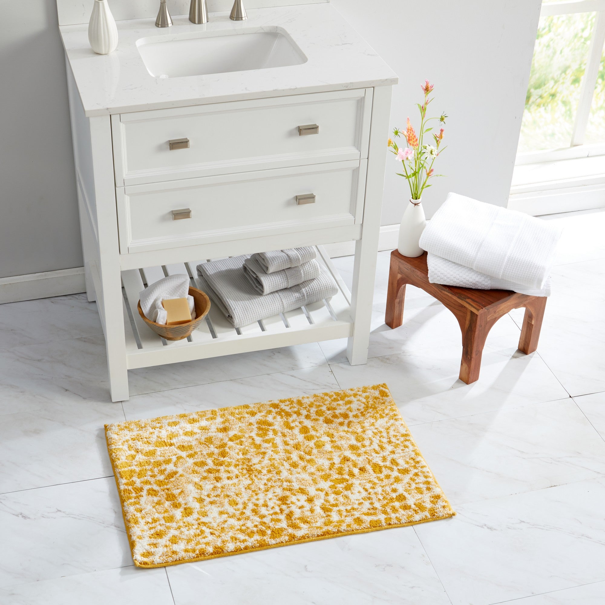 Mustard yellow and ivory cheetah-print bath rug styled in a bright, modern bathroom beside a white vanity and folded towels. The plush rug adds a vibrant animal-inspired accent while providing soft, absorbent comfort and a cozy feel underfoot for everyday use.