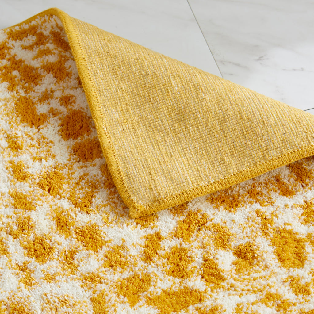 Close-up of a mustard yellow and ivory cheetah-print bath rug with a folded corner revealing the durable woven backing. The plush, textured surface showcases the rug’s soft feel, quality craftsmanship, and absorbent design for everyday bathroom comfort.
