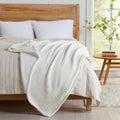 Off-white Maria Collection cotton muslin sherpa throw blanket draped across a bed, showcasing the textured cotton muslin face and soft sherpa backing in a bright bedroom setting.