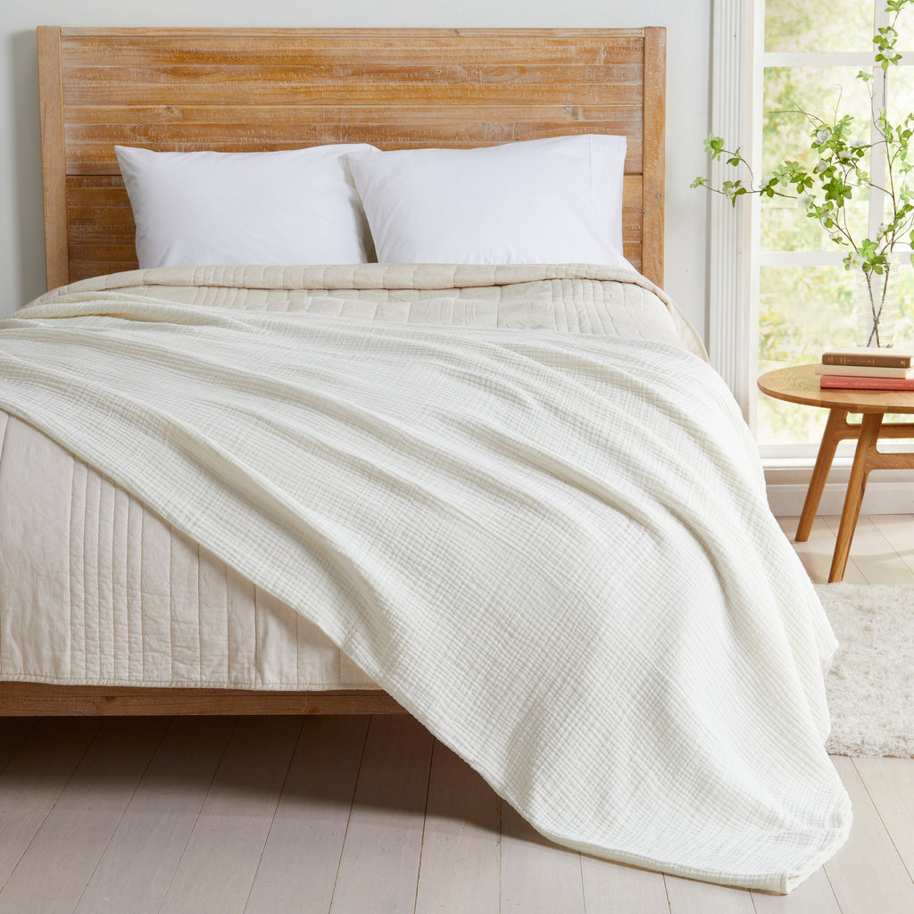 Off-White Maria Collection cotton muslin blanket draped across a bed, showcasing its soft gauze texture, lightweight construction, and relaxed casual style. The breathable cotton blanket adds cozy comfort and a clean, modern touch to the bedroom décor.