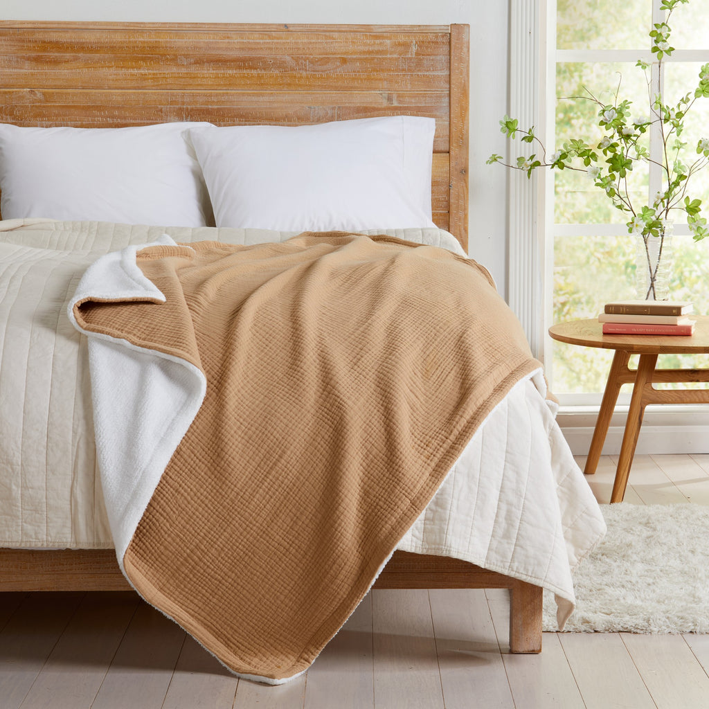 Beige Maria Collection cotton muslin sherpa throw blanket draped across a bed, showcasing the textured cotton muslin face and plush sherpa backing in a bright bedroom setting.