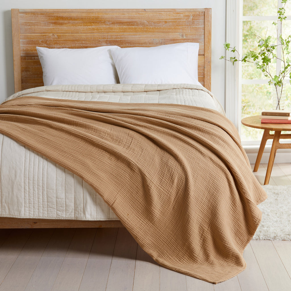Beige Maria Collection cotton muslin blanket draped across a bed, showcasing its soft textured muslin weave and lightweight construction that brings warmth, comfort, and relaxed style to any bedroom décor.