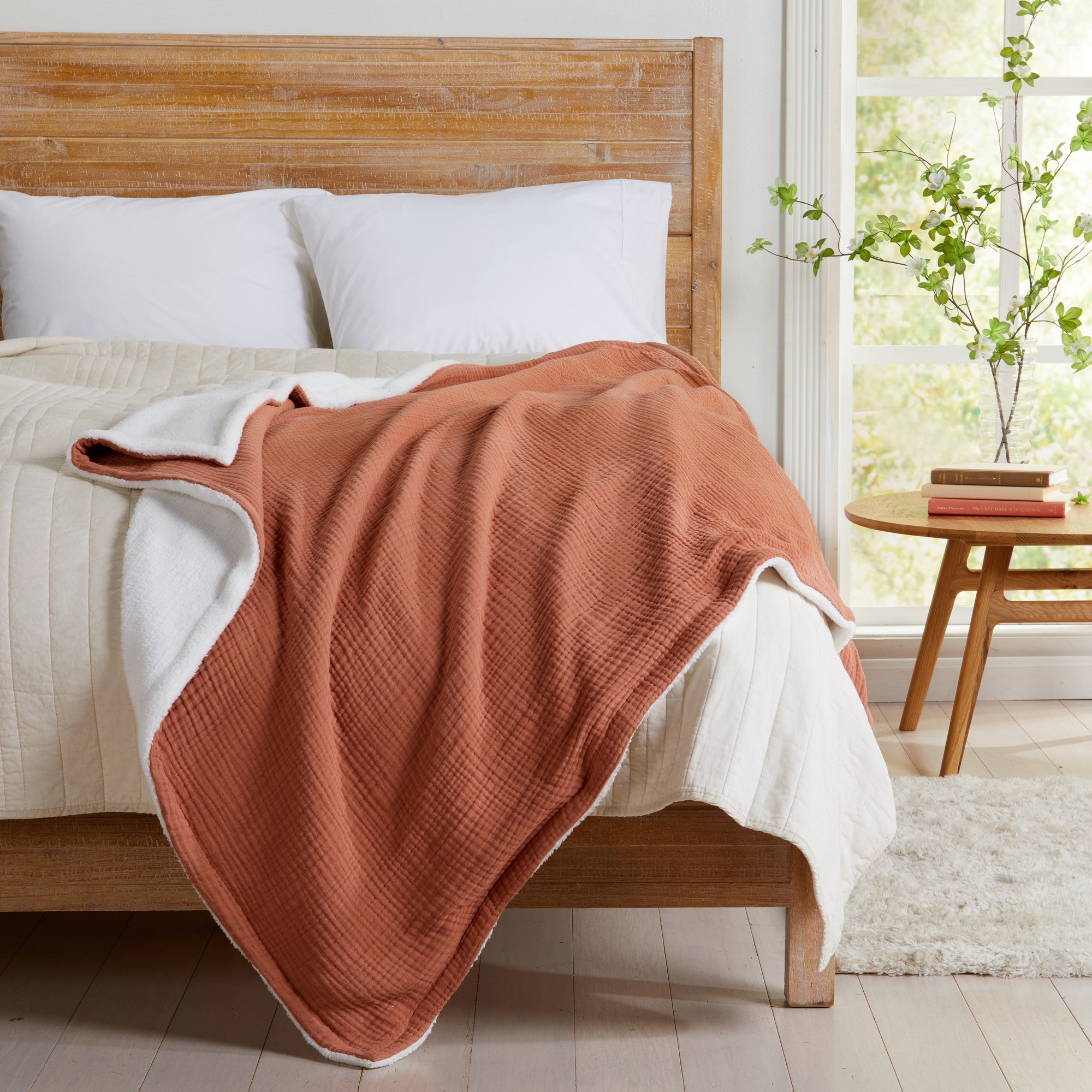 Rust Maria Collection cotton muslin sherpa throw blanket draped across a bed, showcasing the textured cotton muslin face and plush sherpa backing in a bright bedroom setting.