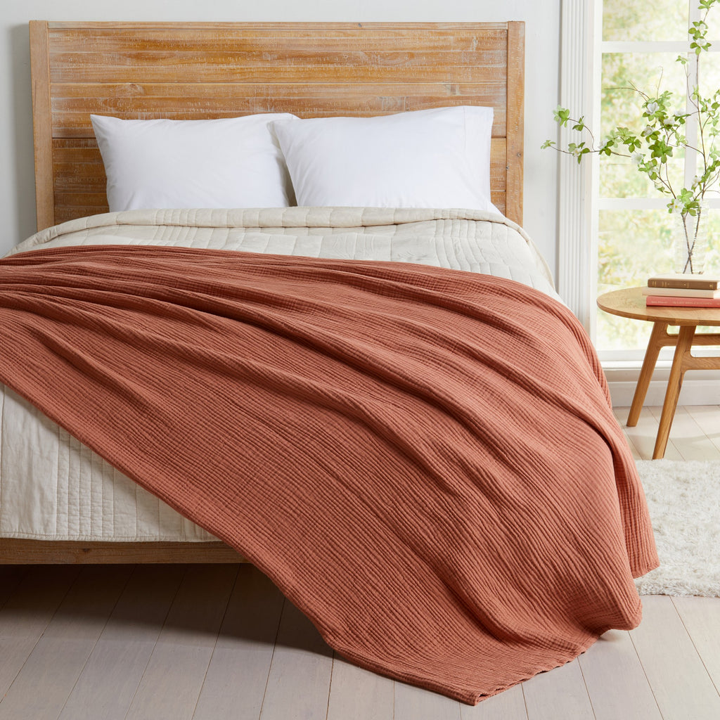 Rust Maria Collection cotton muslin blanket draped across a bed, featuring a soft textured muslin weave and lightweight design that adds warmth, comfort, and inviting style to any bedroom setting.