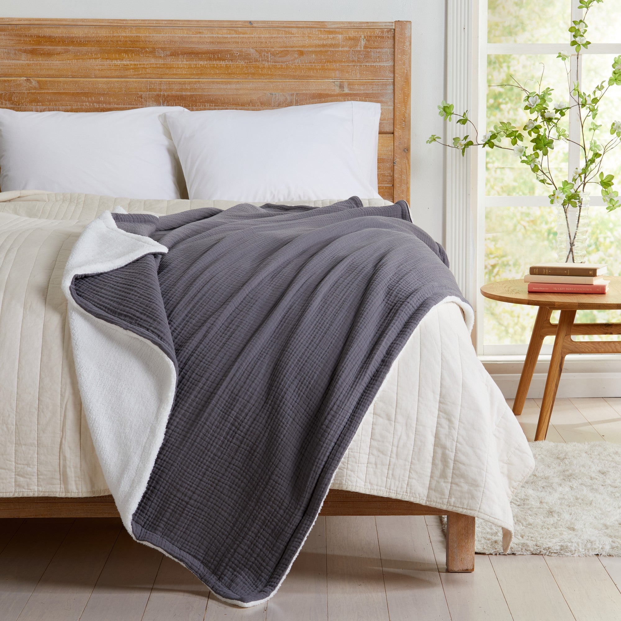 Charcoal Maria Collection cotton muslin sherpa throw blanket draped across a bed, showcasing the textured cotton muslin face and plush sherpa backing in a bright bedroom setting.
