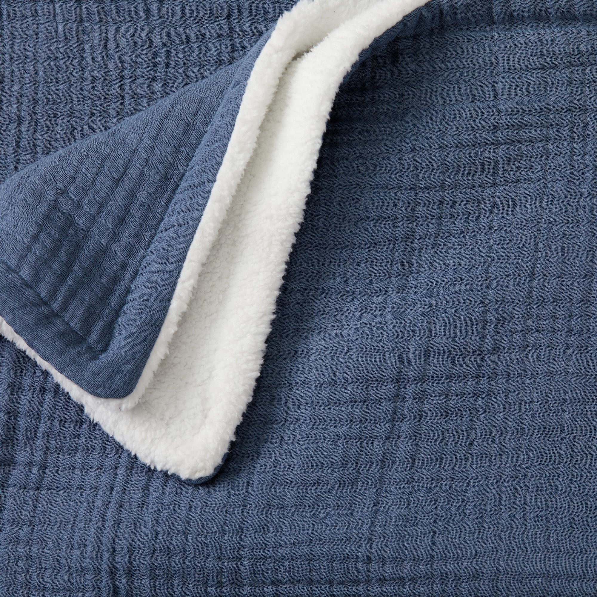 Close-up of the Blue Maria Collection cotton muslin sherpa throw blanket, highlighting the soft gauze-like cotton muslin texture and plush sherpa backing for cozy comfort and warmth.