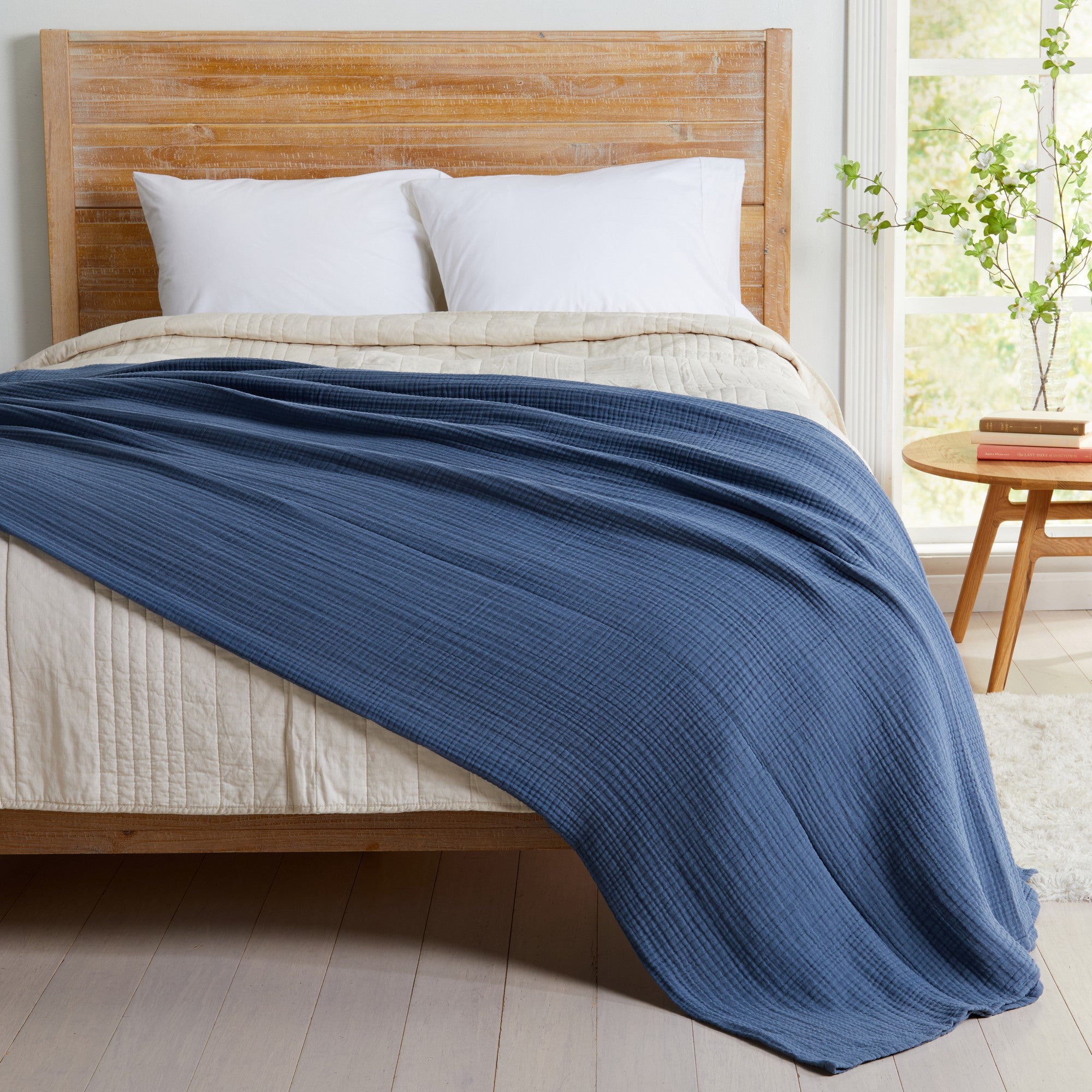 Blue Maria Collection cotton muslin blanket draped across a bed, showcasing its soft textured muslin weave and lightweight design that provides breathable comfort and relaxed, coastal-inspired style.