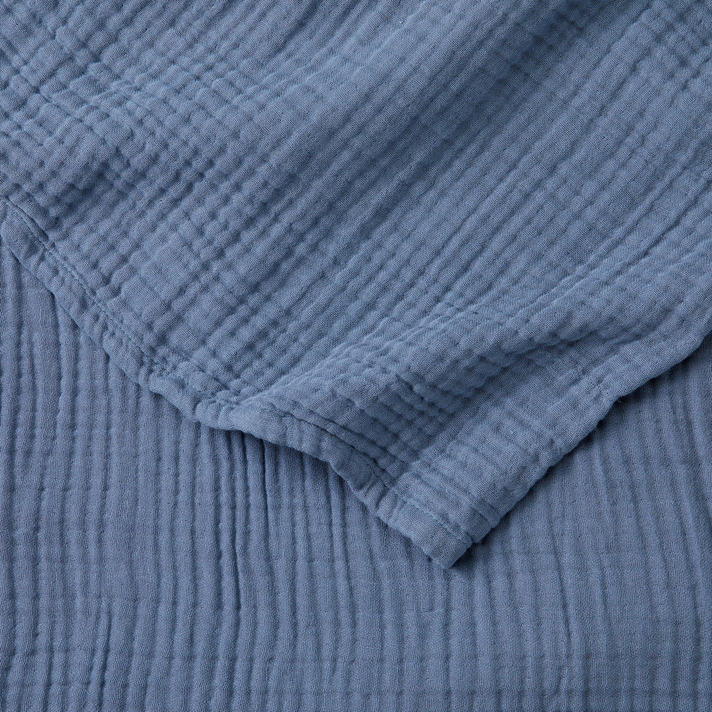 Close-up detail of the Blue Maria Collection cotton muslin blanket showcasing its soft gauze texture, breathable multi-layer weave, and calming blue color. The image highlights the blanket’s lightweight construction, natural crinkled finish, and relaxed contemporary style.