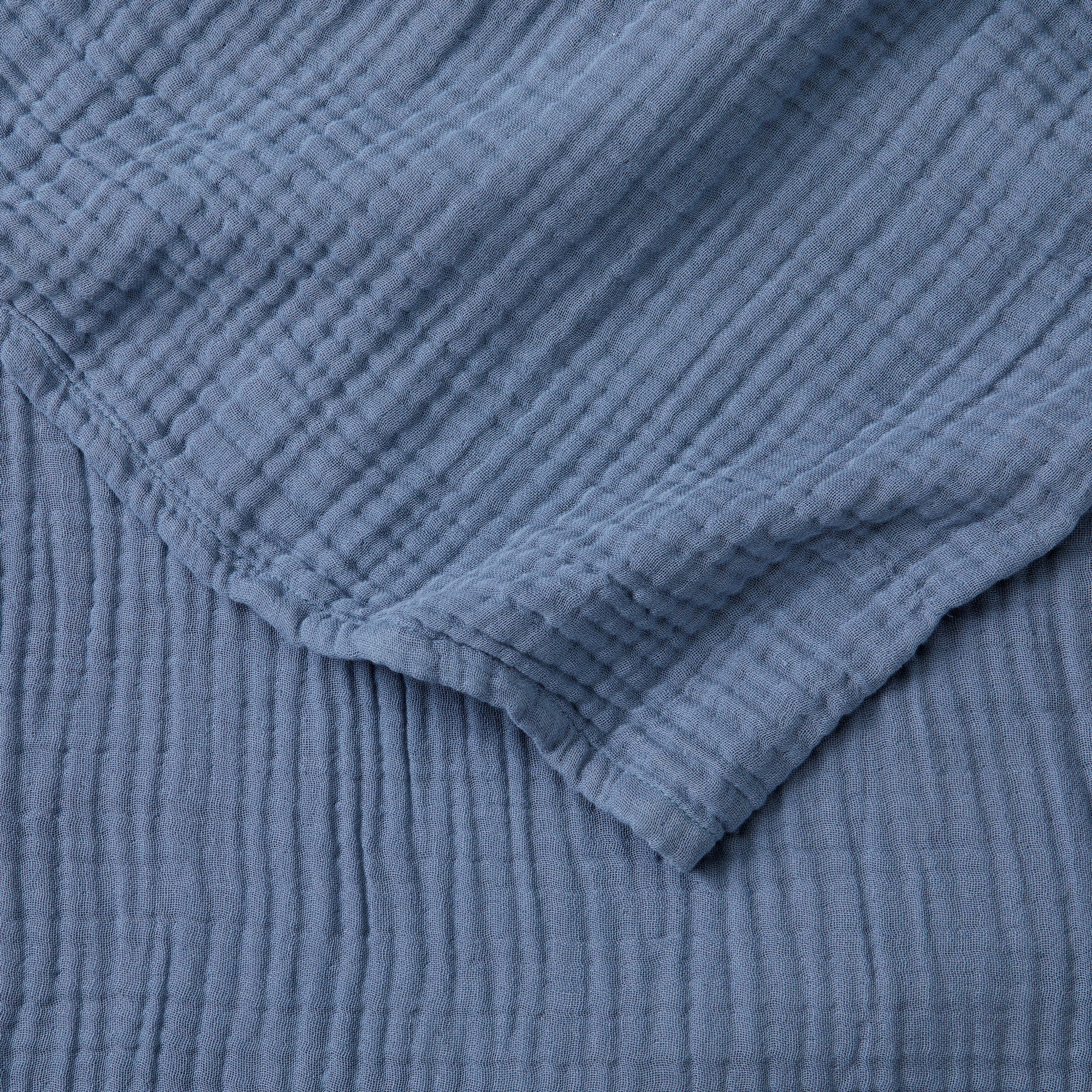Close-up detail of the Blue Maria Collection cotton muslin blanket showcasing its soft gauze texture, breathable multi-layer weave, and calming blue color. The image highlights the blanket’s lightweight construction, natural crinkled finish, and relaxed contemporary style.
