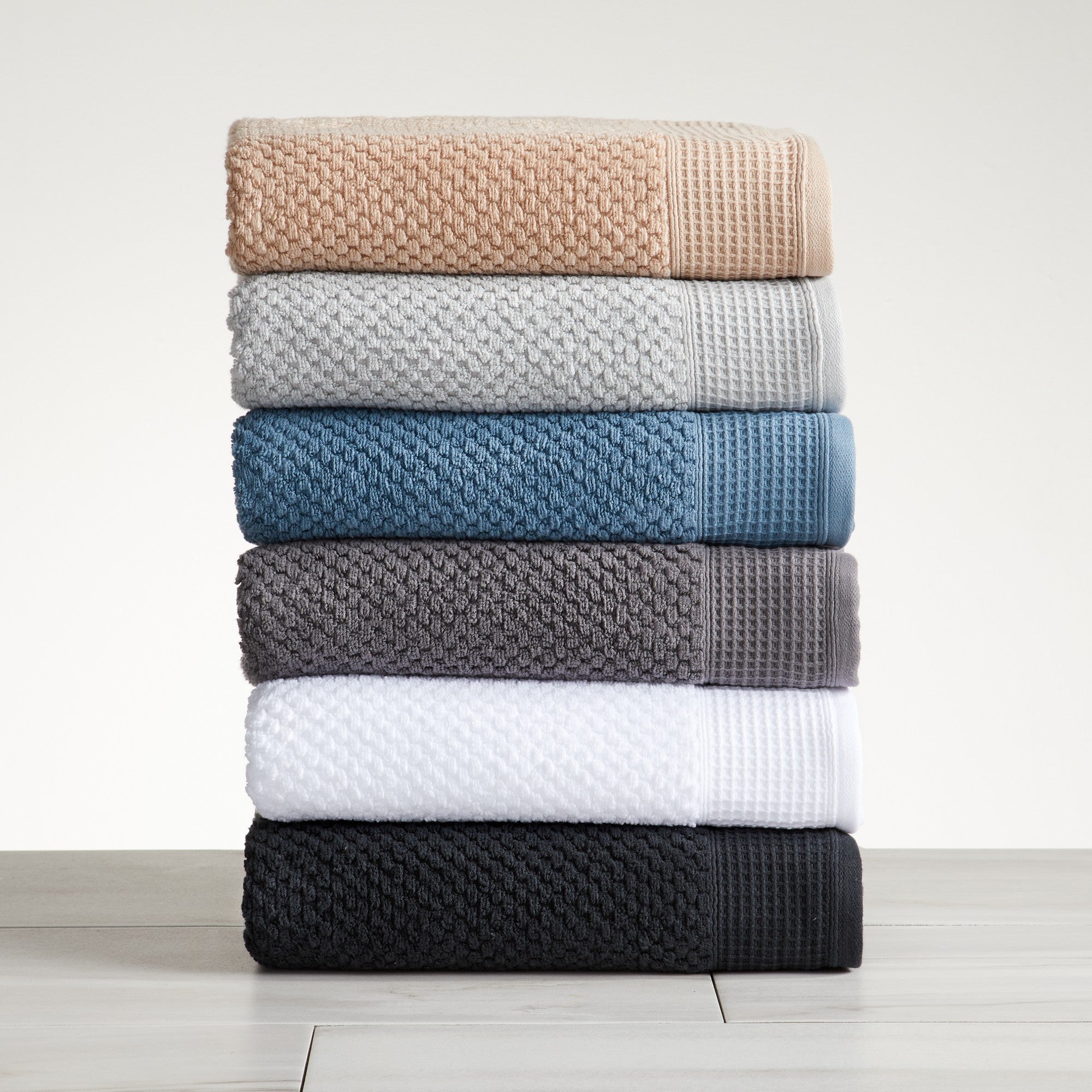 A stack of folded bath towels, hand towels, and washcloths in various solid colors on a wooden surface.