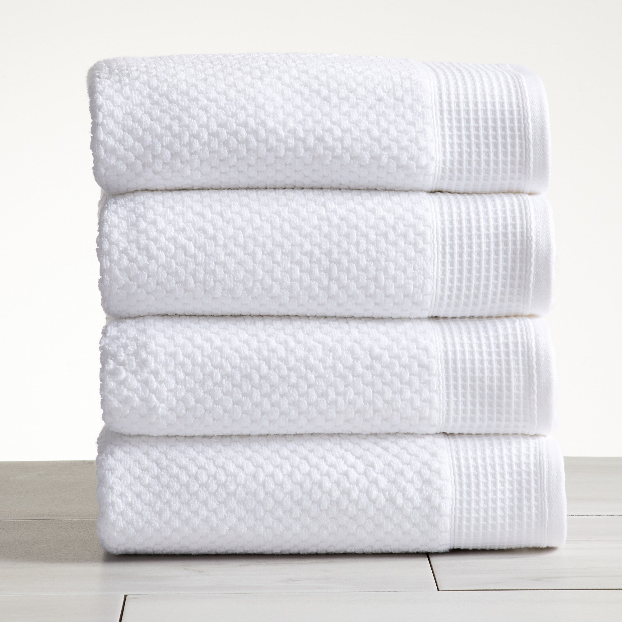 White cotton bath towels folded and stacked on white surface