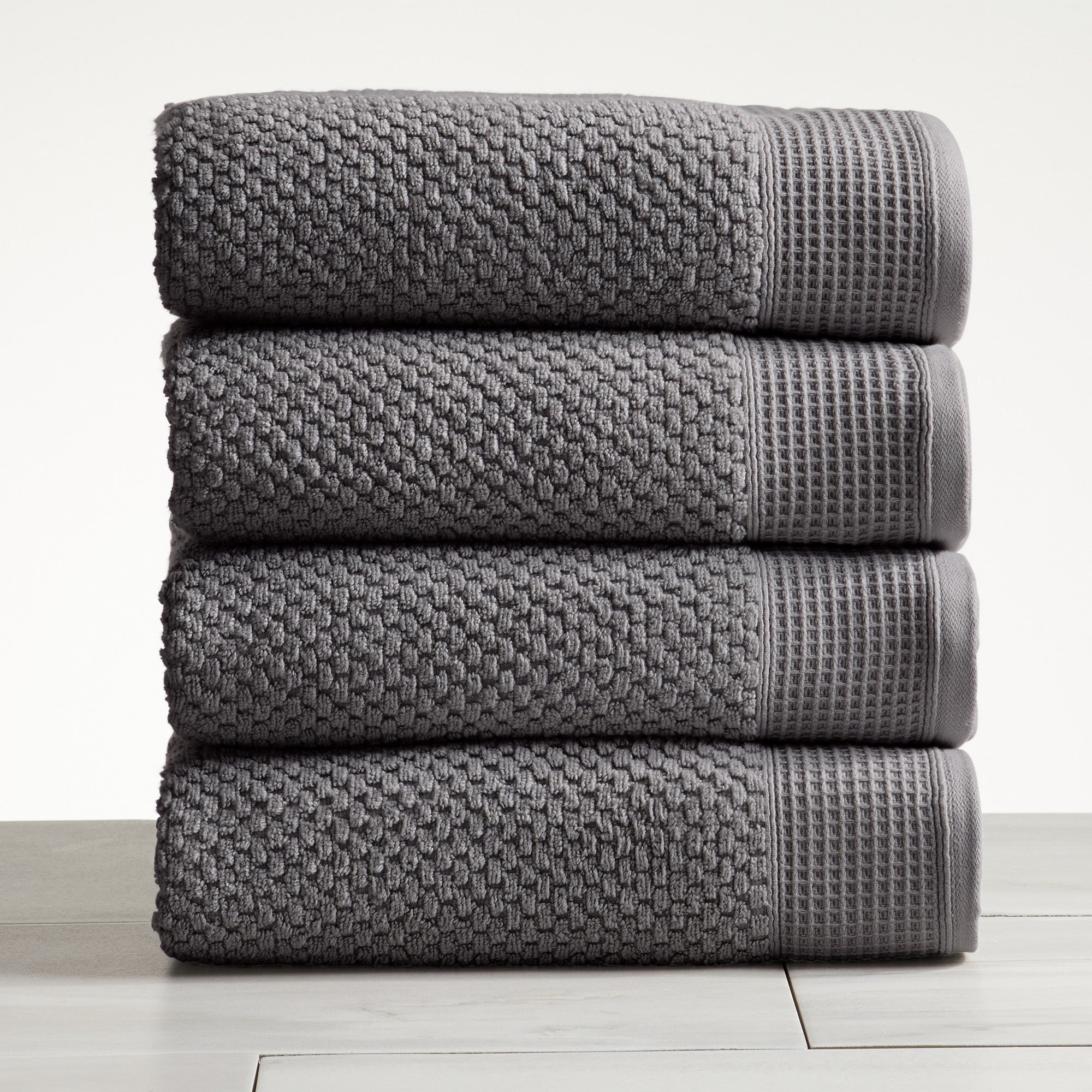 Gray cotton bath towels folded and stacked on white surface