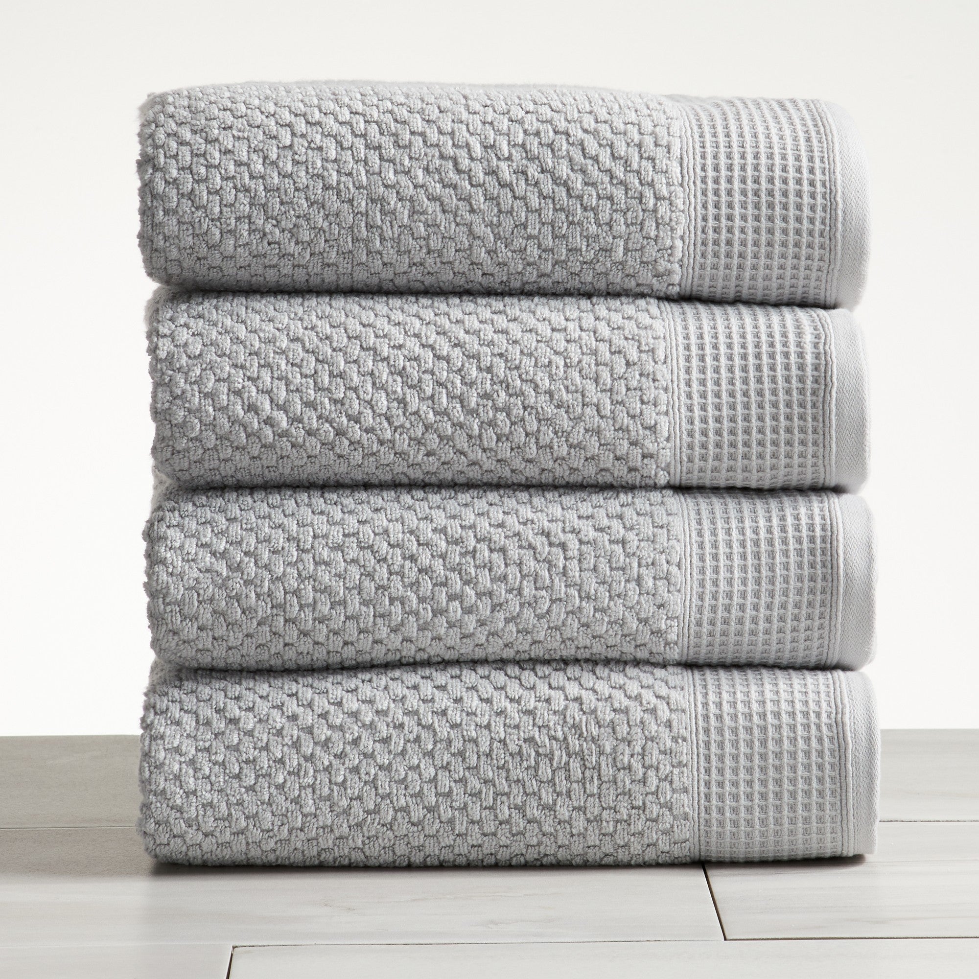 Light gray cotton bath towels folded and stacked on white surface