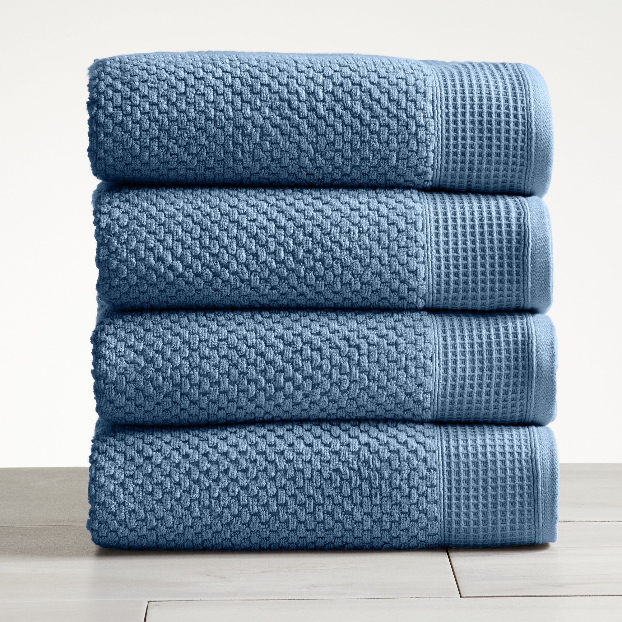Blue cotton bath towels folded and stacked on white surface