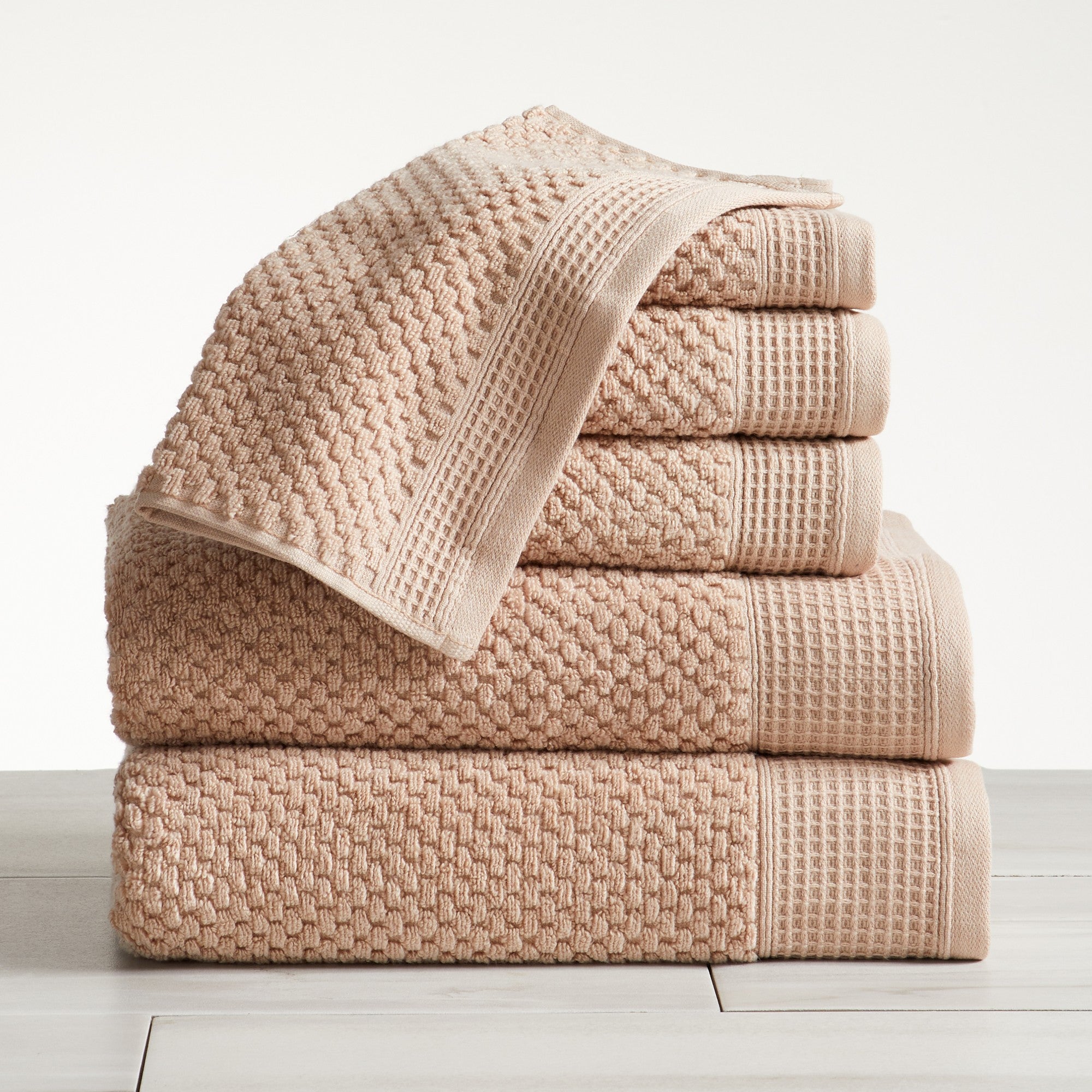 Beige cotton bath towels folded and stacked on white surface