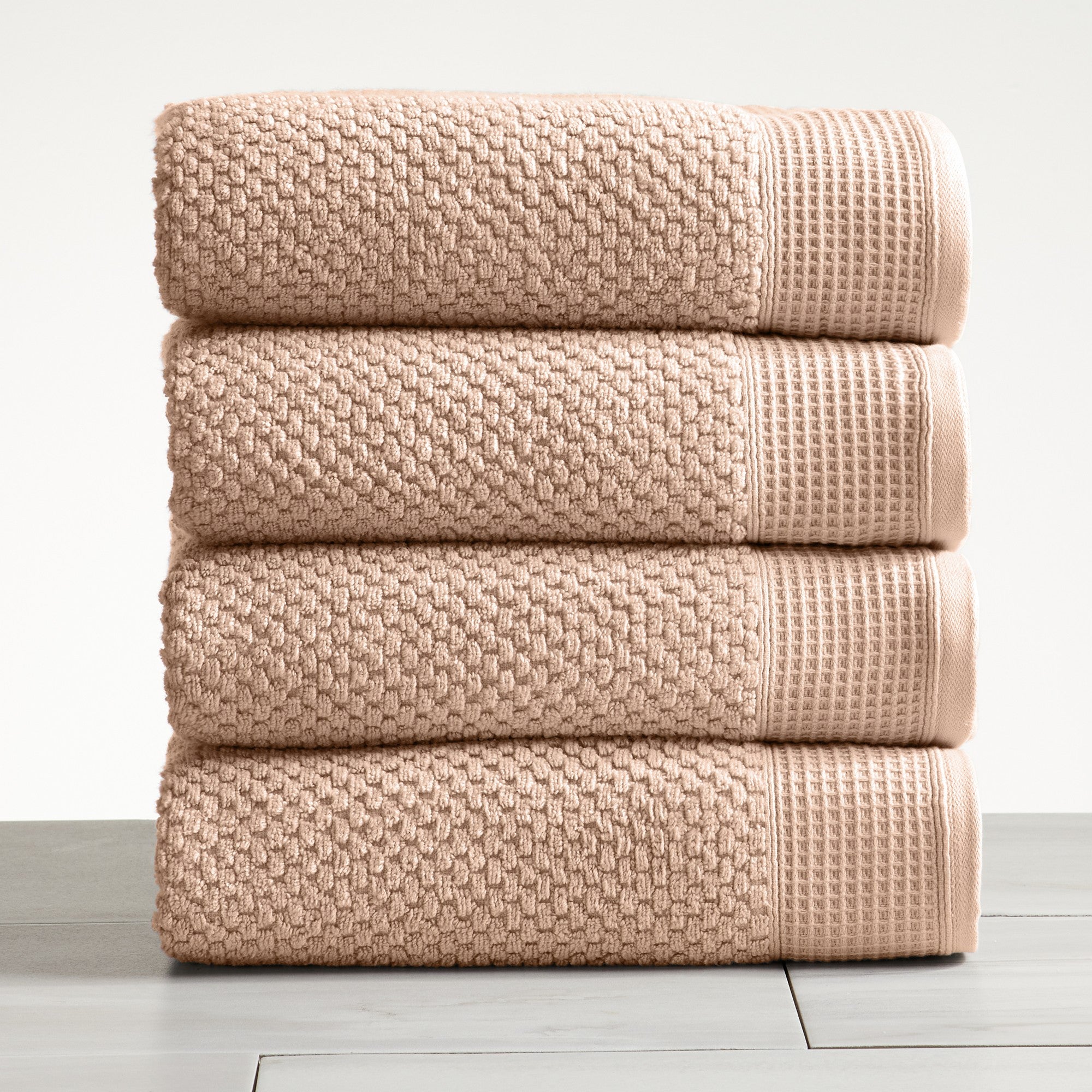 Beige cotton bath towels folded and stacked on white surface
