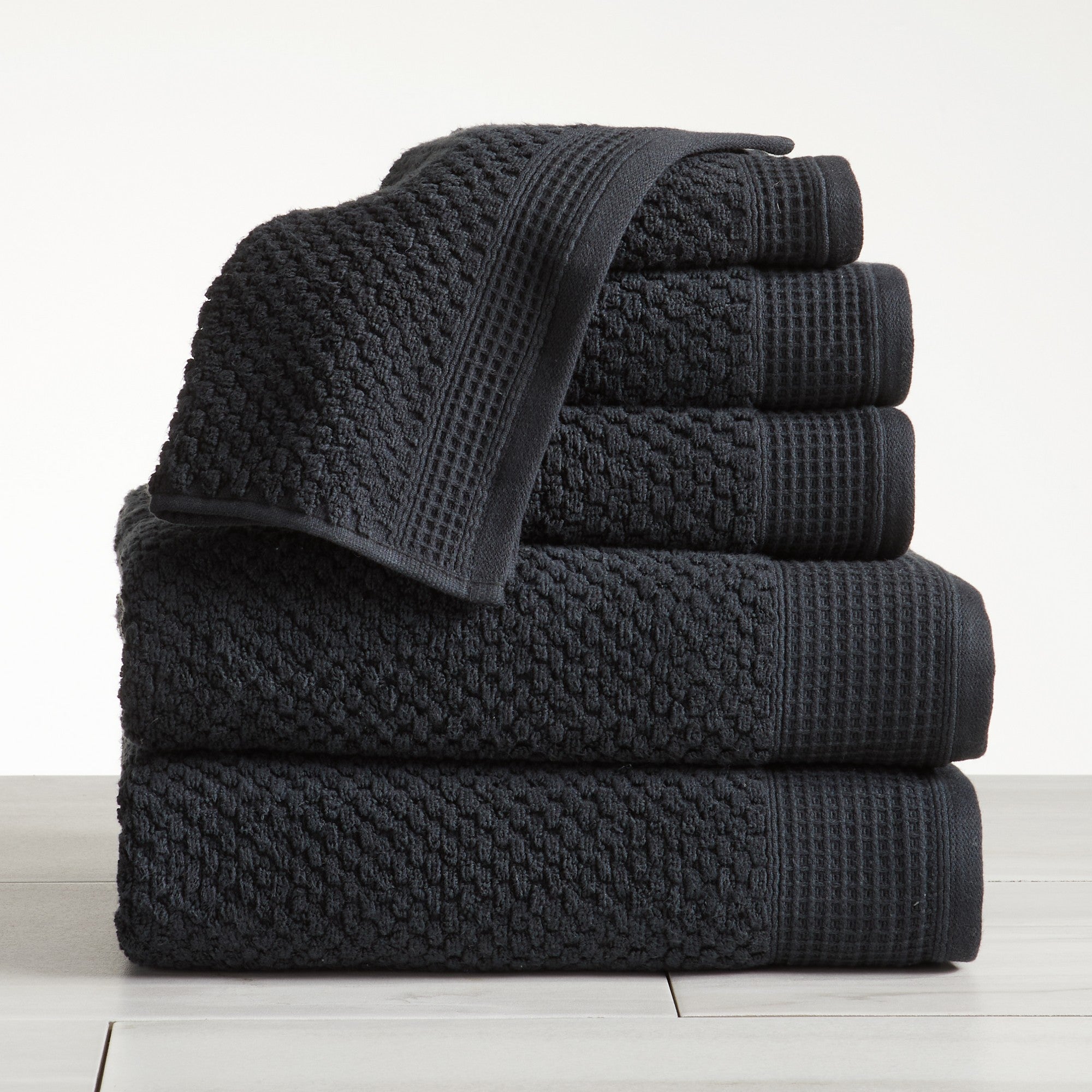 Black cotton bath towels folded and stacked on white surface