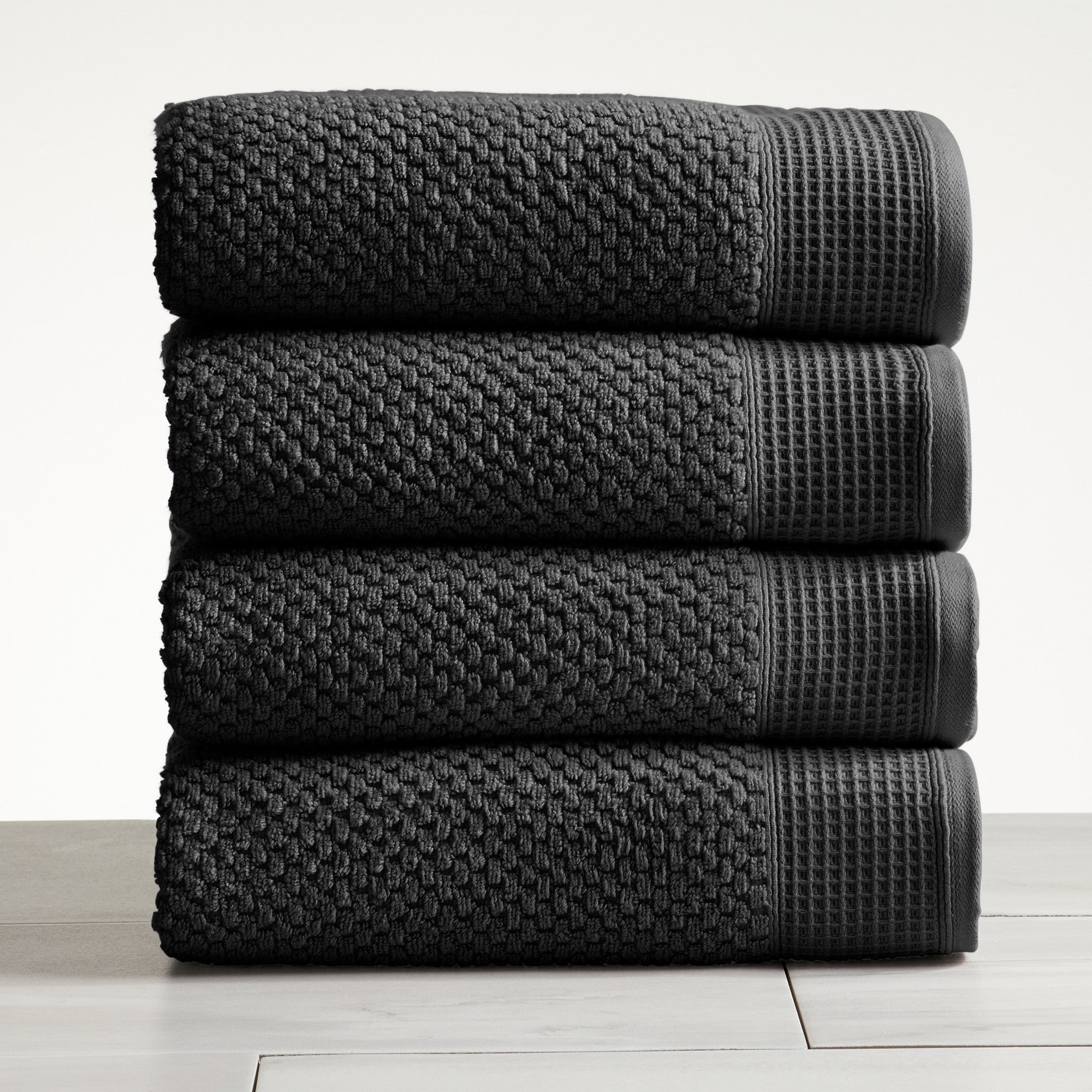 Black cotton bath towels folded and stacked on white surface
