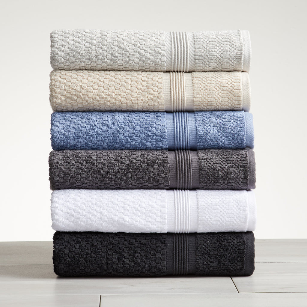 A set of folded bath towels, hand towels, and washcloths in various solid colors stacked on a wooden surface.