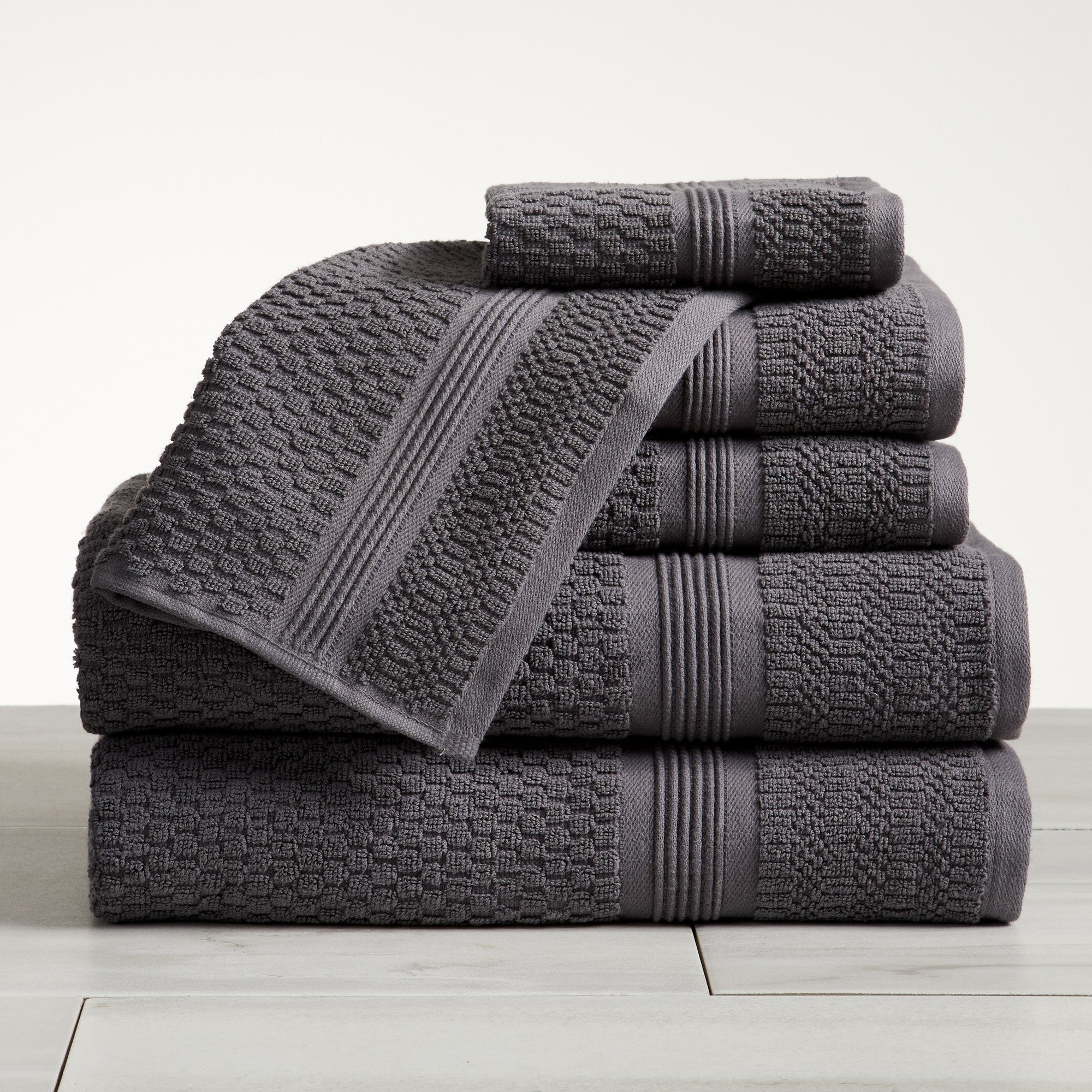 Gray waffle weave cotton bath towel set stacked on white surface