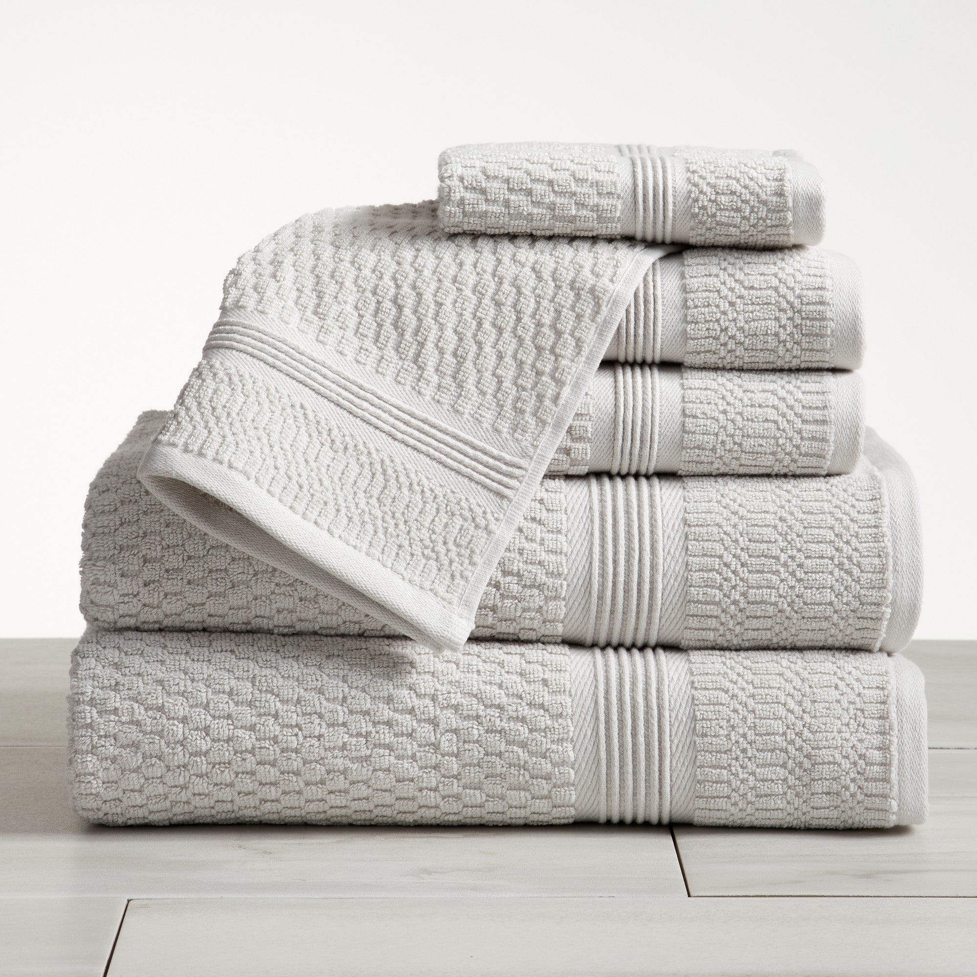 Light gray waffle weave cotton bath towel set stacked on white surface
