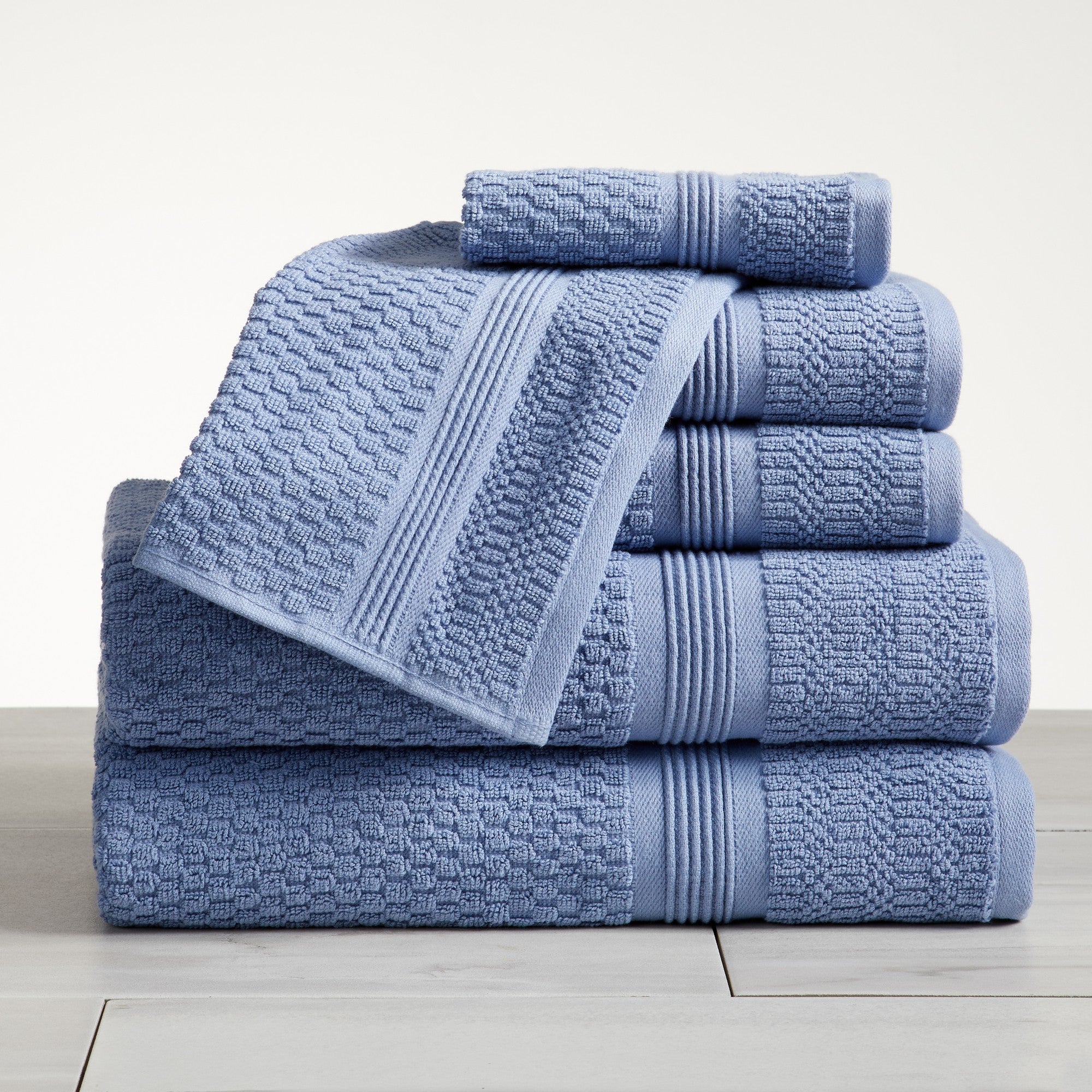 Blue waffle weave cotton bath towel set stacked on white surface