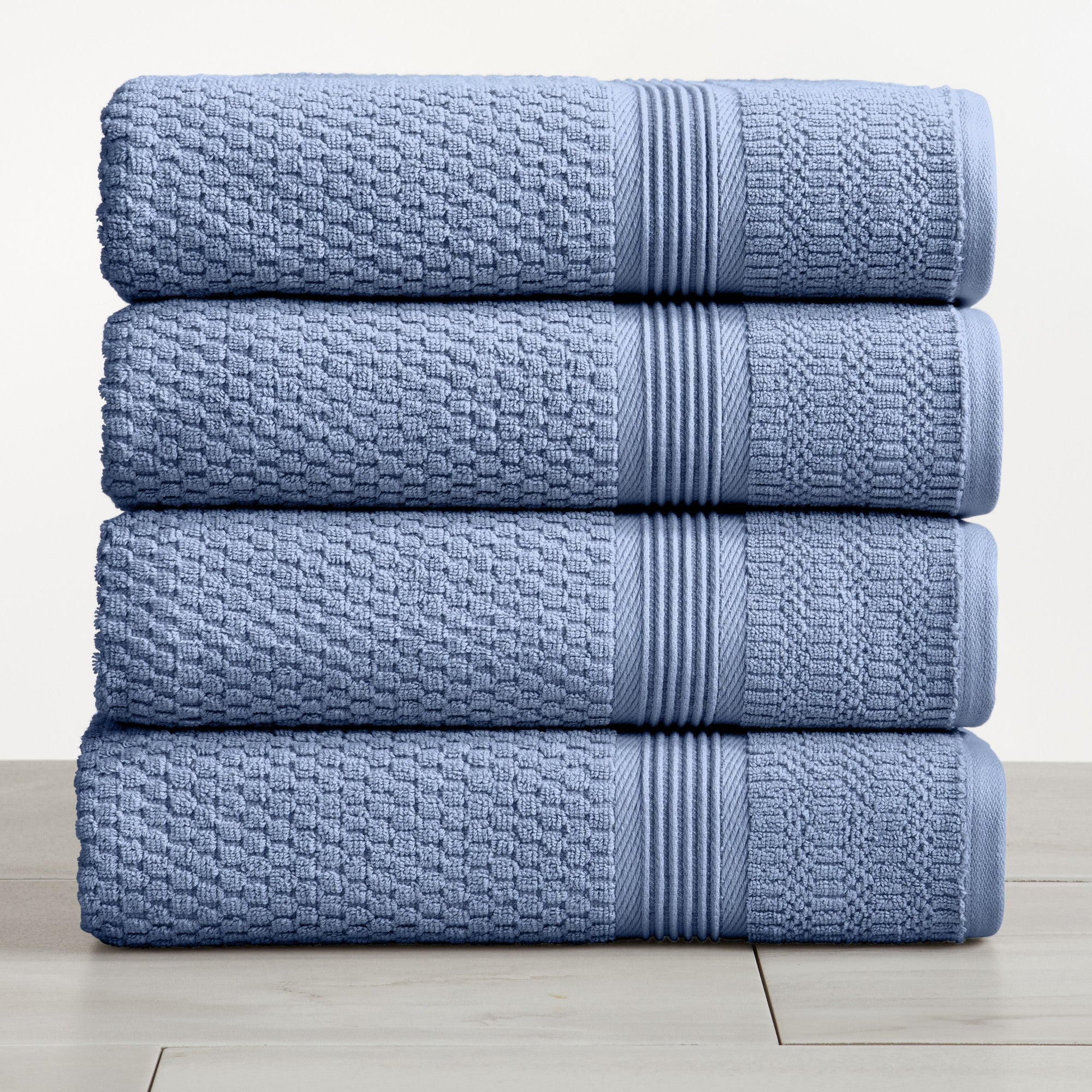Blue waffle weave cotton bath towels stacked on white surface