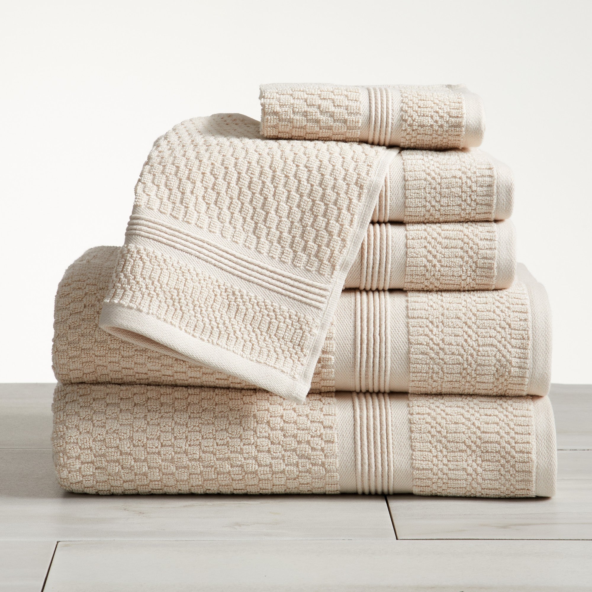 Beige waffle weave cotton bath towel set stacked on white surface