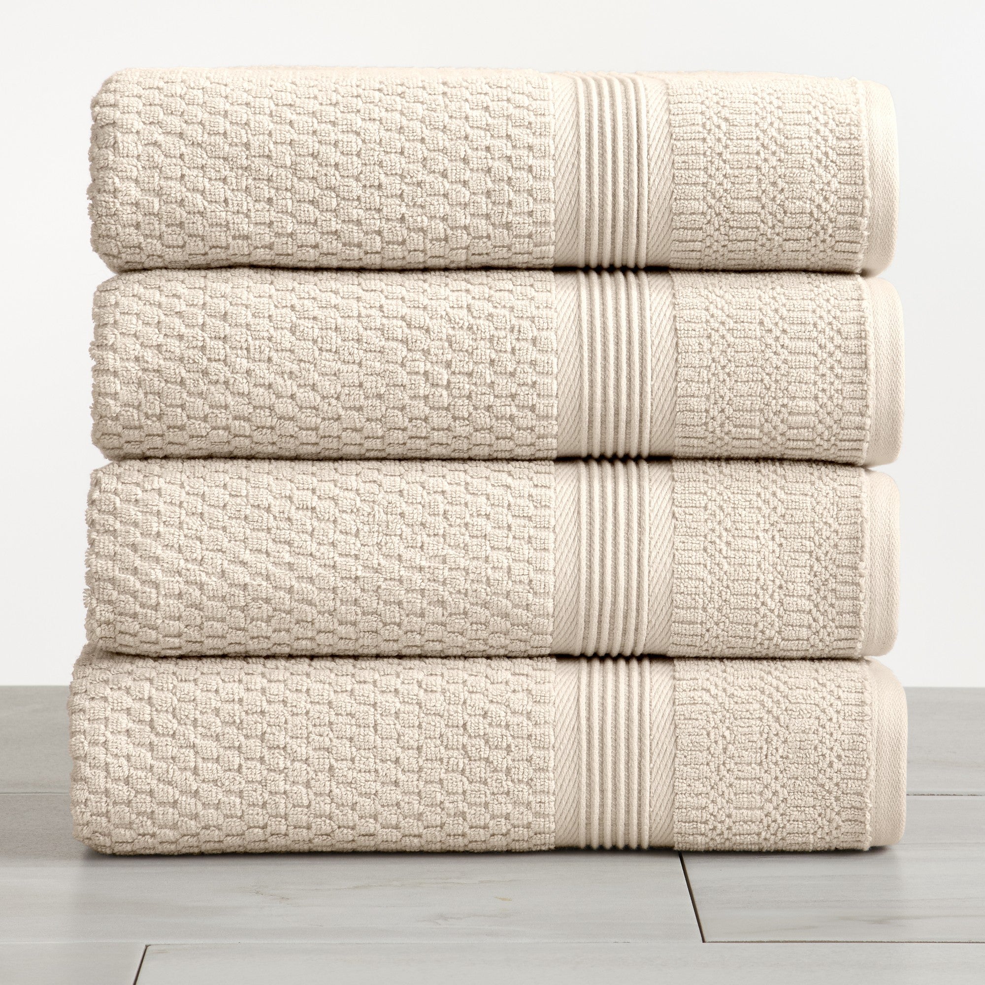 Beige waffle weave cotton bath towels stacked on white surface