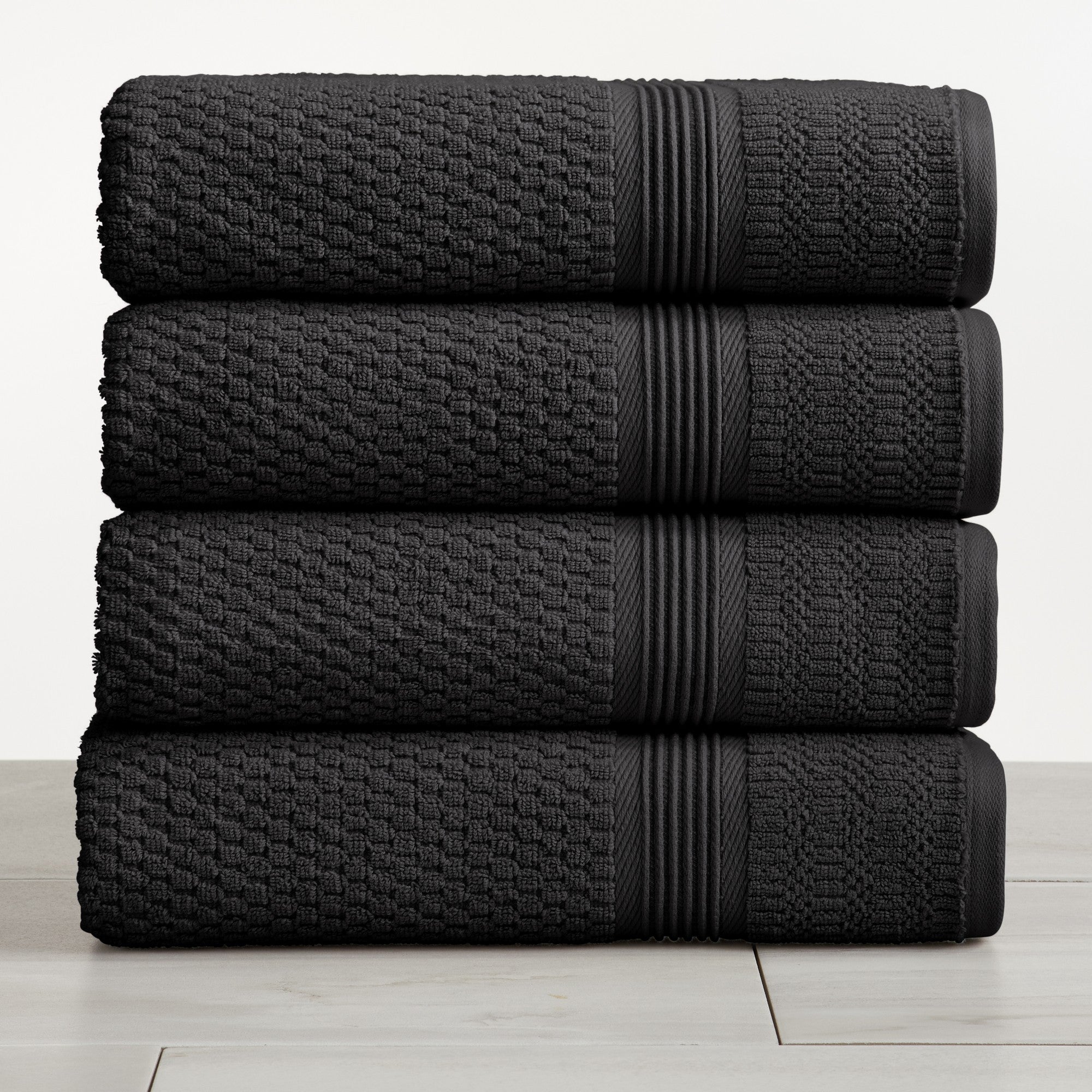 Black waffle weave cotton bath towels stacked on white surface