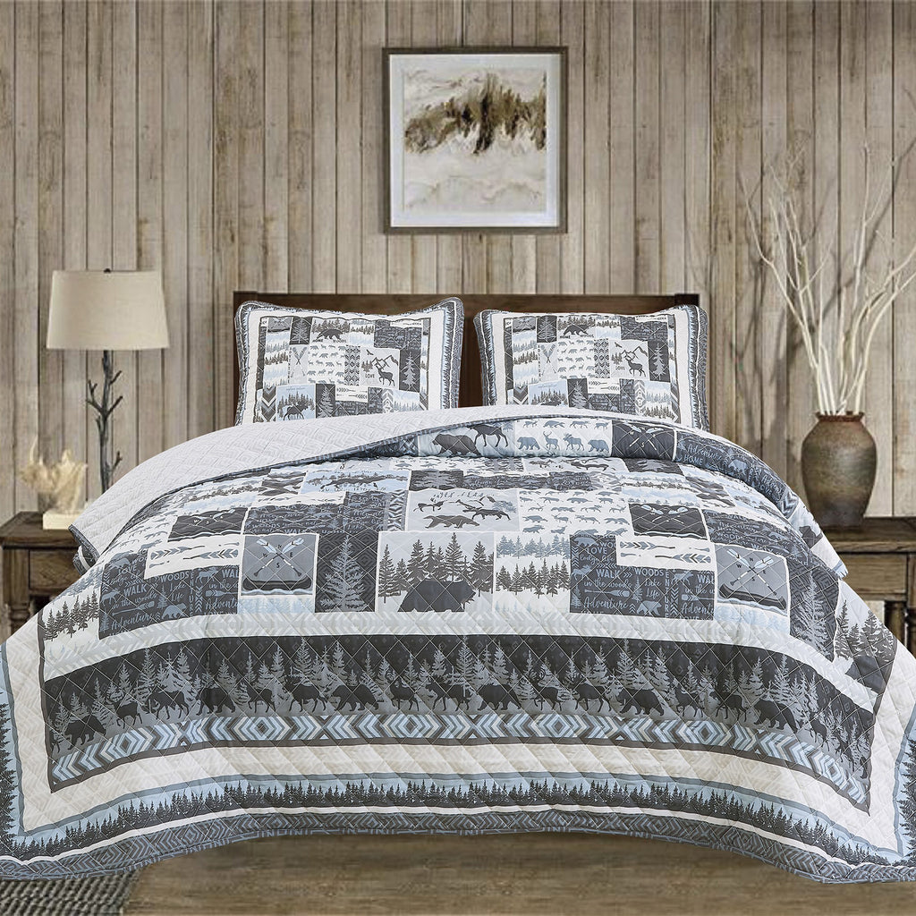 A quilt set with a cabin theme, featuring moose, bears, and trees, displayed on a bed in a room with a wooden bed frame and a decorative lamp.