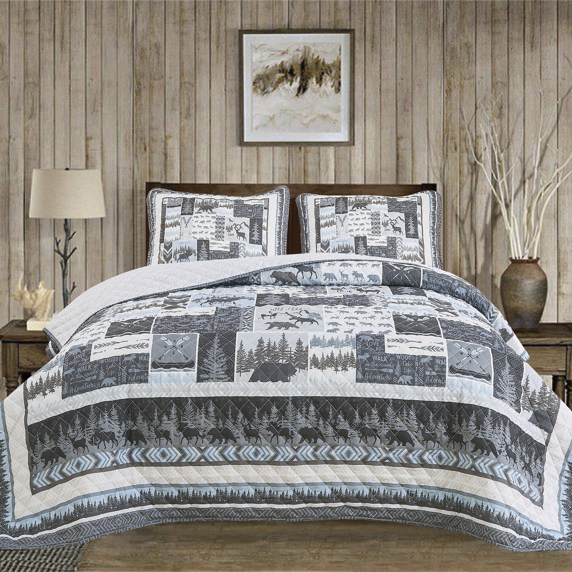 A quilt set with a cabin theme, featuring moose, bears, and trees, displayed on a bed in a room with a wooden bed frame and a decorative lamp.