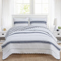 A reversible striped quilt set with a modern design, featuring navy and white stripes, displayed on a bed with two accompanying pillows. The quilt is draped over the bed with a visible white and navy striped pattern on both sides.