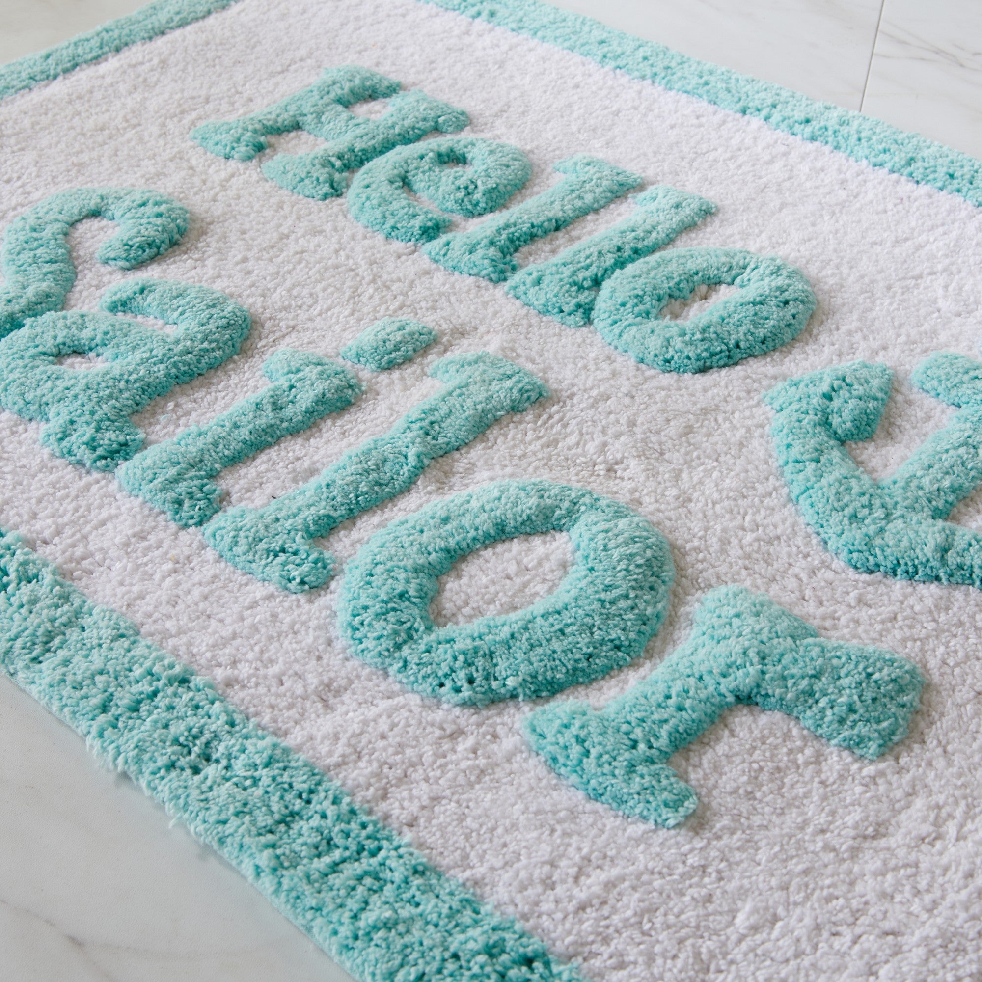 Turquoise bath mat with 'Hello World' text on a white background
