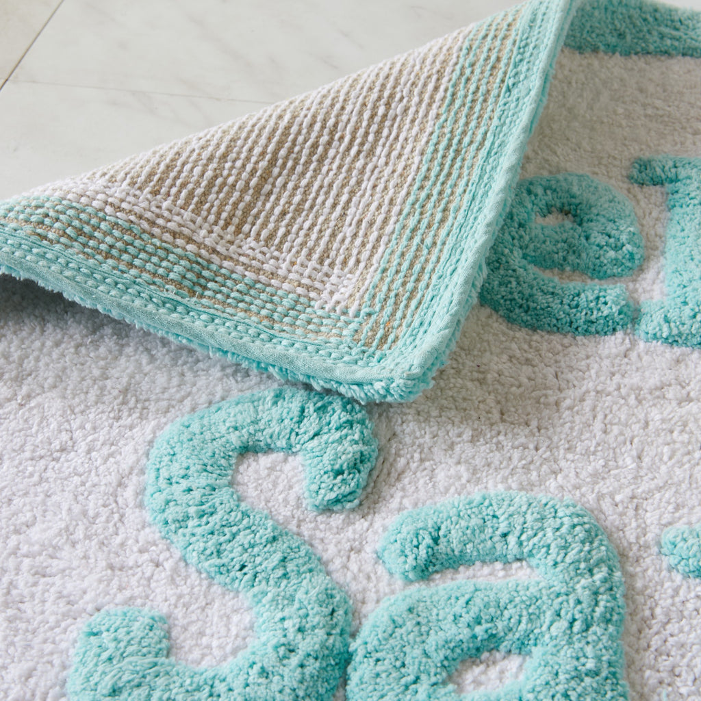 Turquoise textured bath mat with letters on a light gray surface