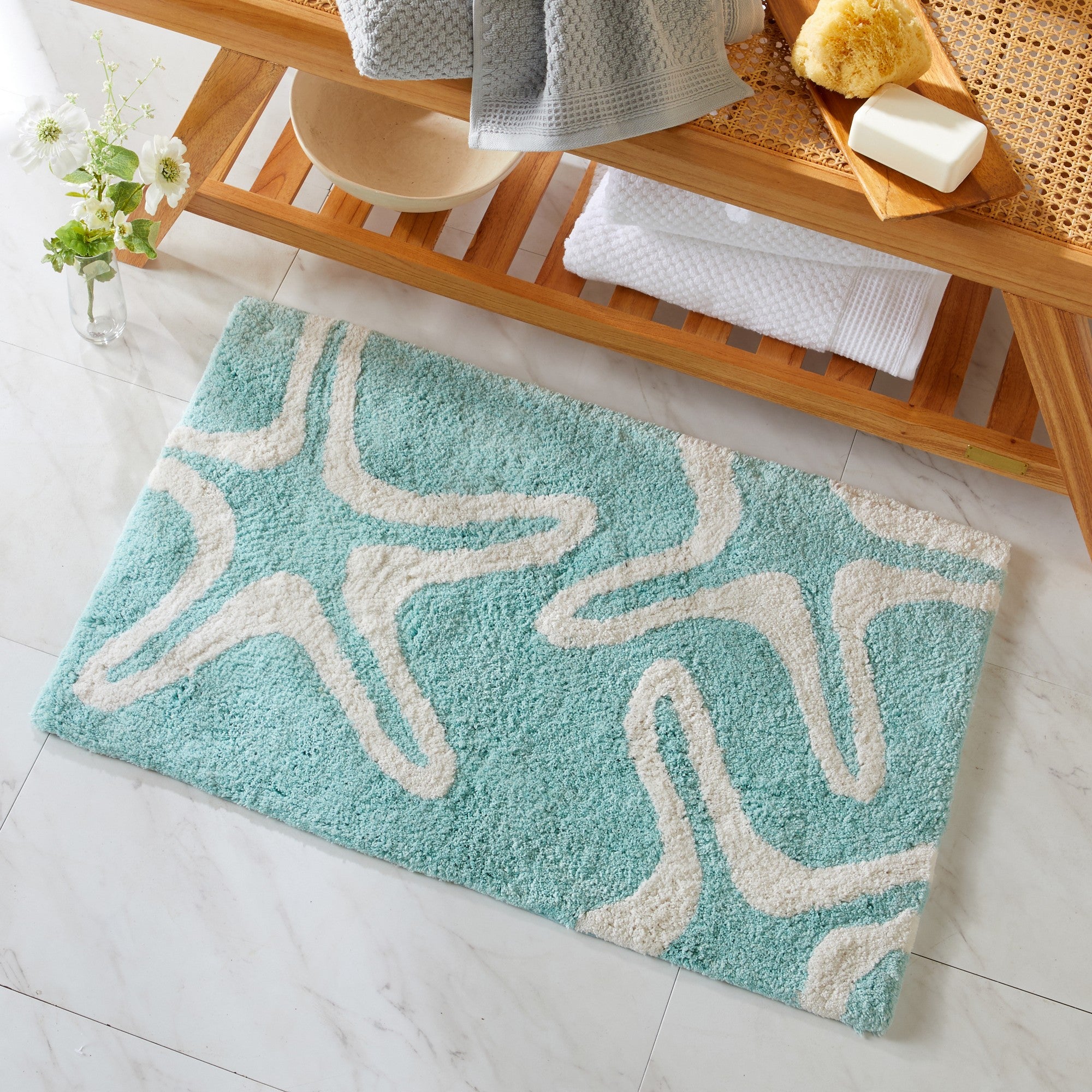 Turquoise bath mat with white patterns on a bathroom floor.