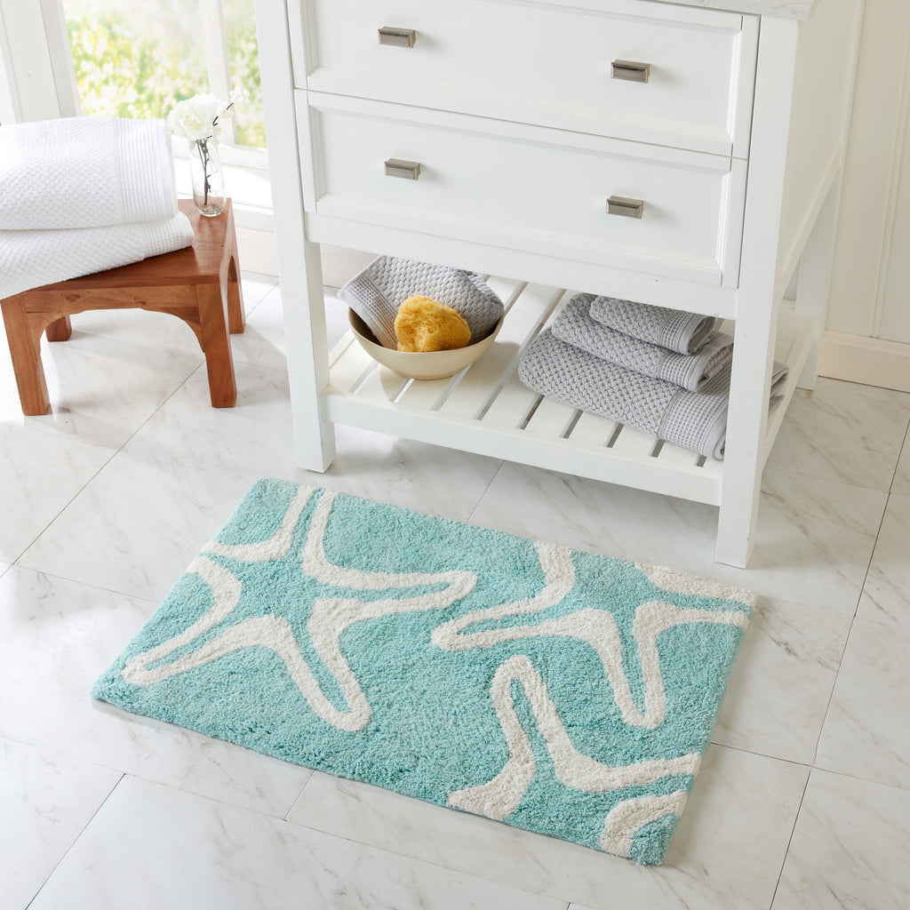 Turquoise bath mat with starfish design on a white tiled floor.