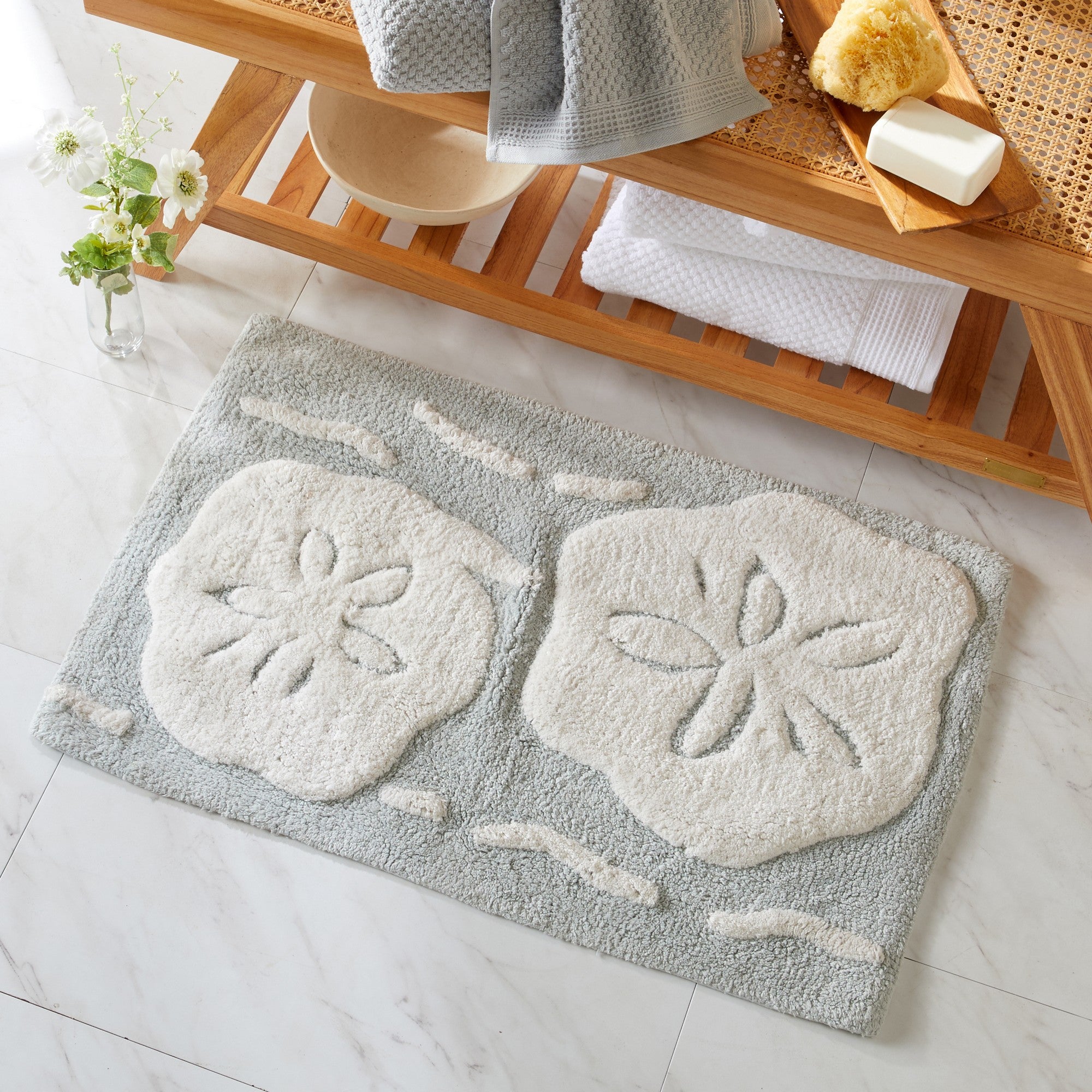 Gray bath mat with white floral patterns on a bathroom floor.