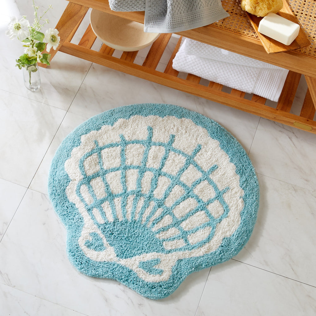 Shell-shaped bath mat on a bathroom floor with a wooden shelf in the background.